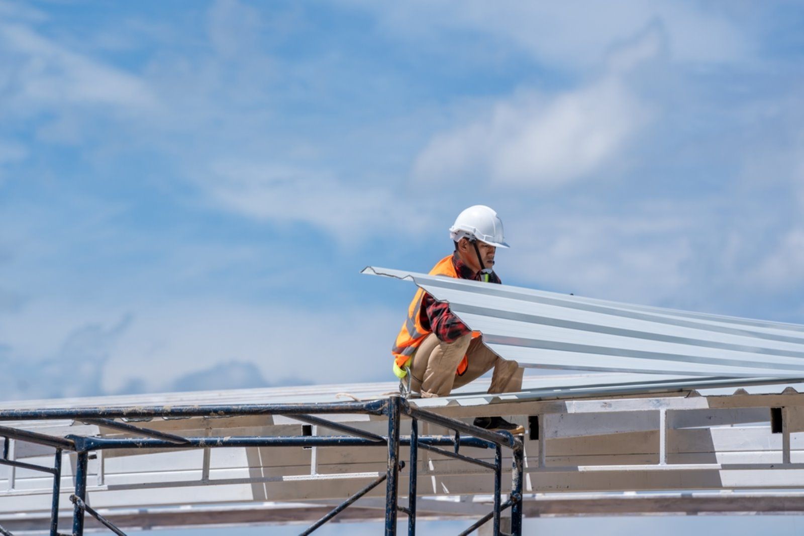 A Construction Worker is Sitting on Top of a Metal Roof — Cairns Roofing Contractors Pty Ltd in Bungalow, QLD