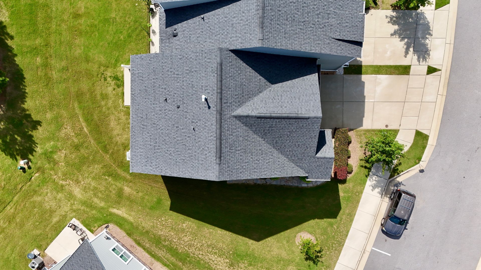 Overhead view of a gray-roofed house surrounded by green grass, with a driveway and road.