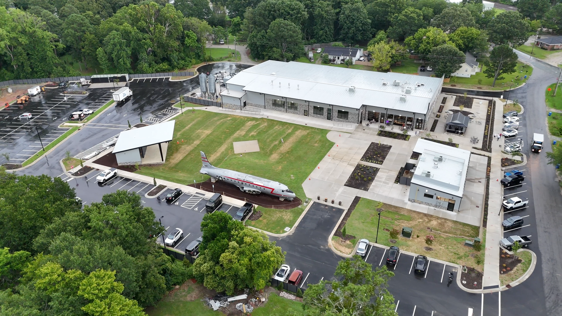 Aerial view of a large industrial building with an airplane display, trees, and parking.