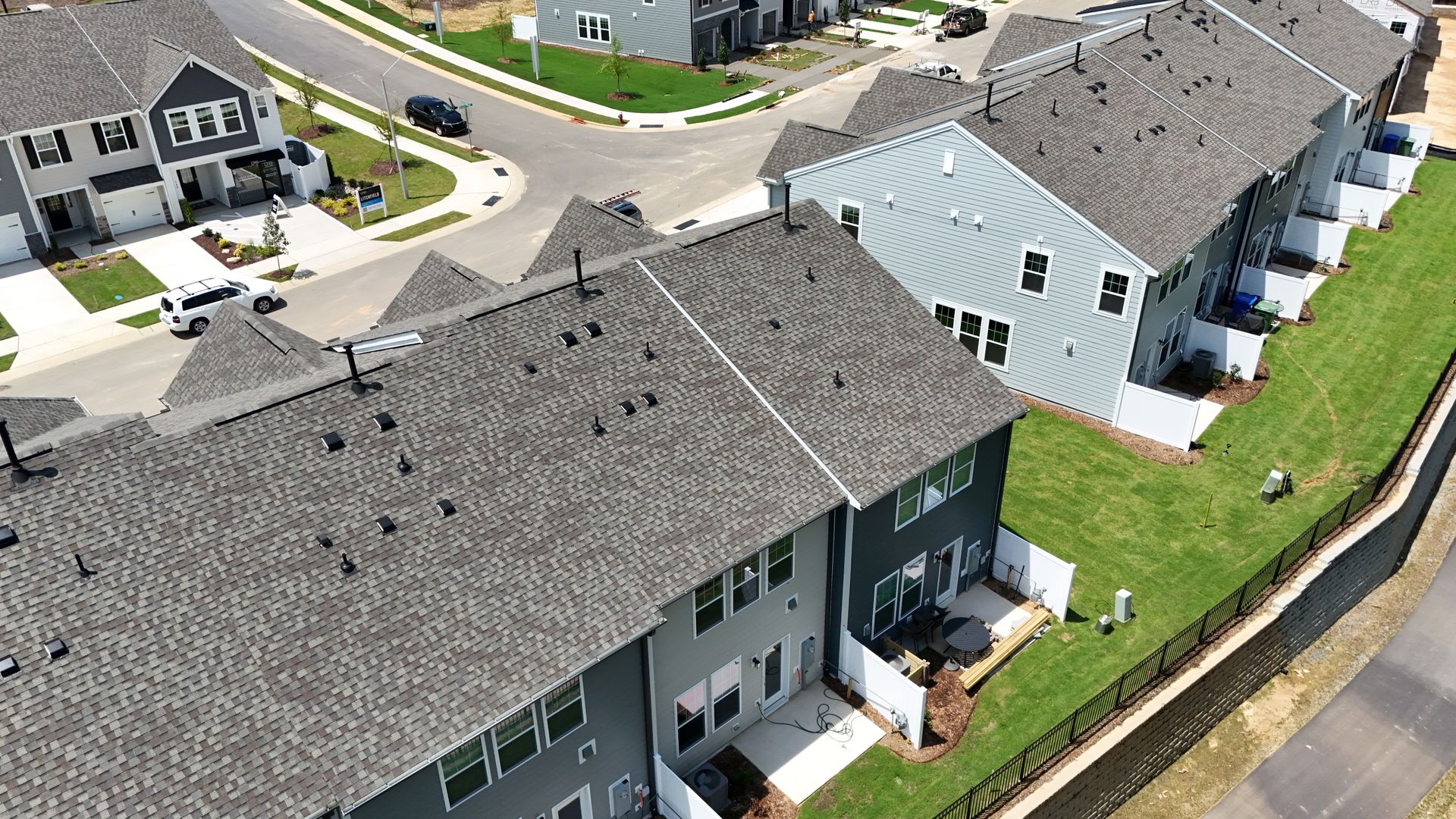 Aerial view of modern townhouses with gray siding, brown roofs, and green lawns.