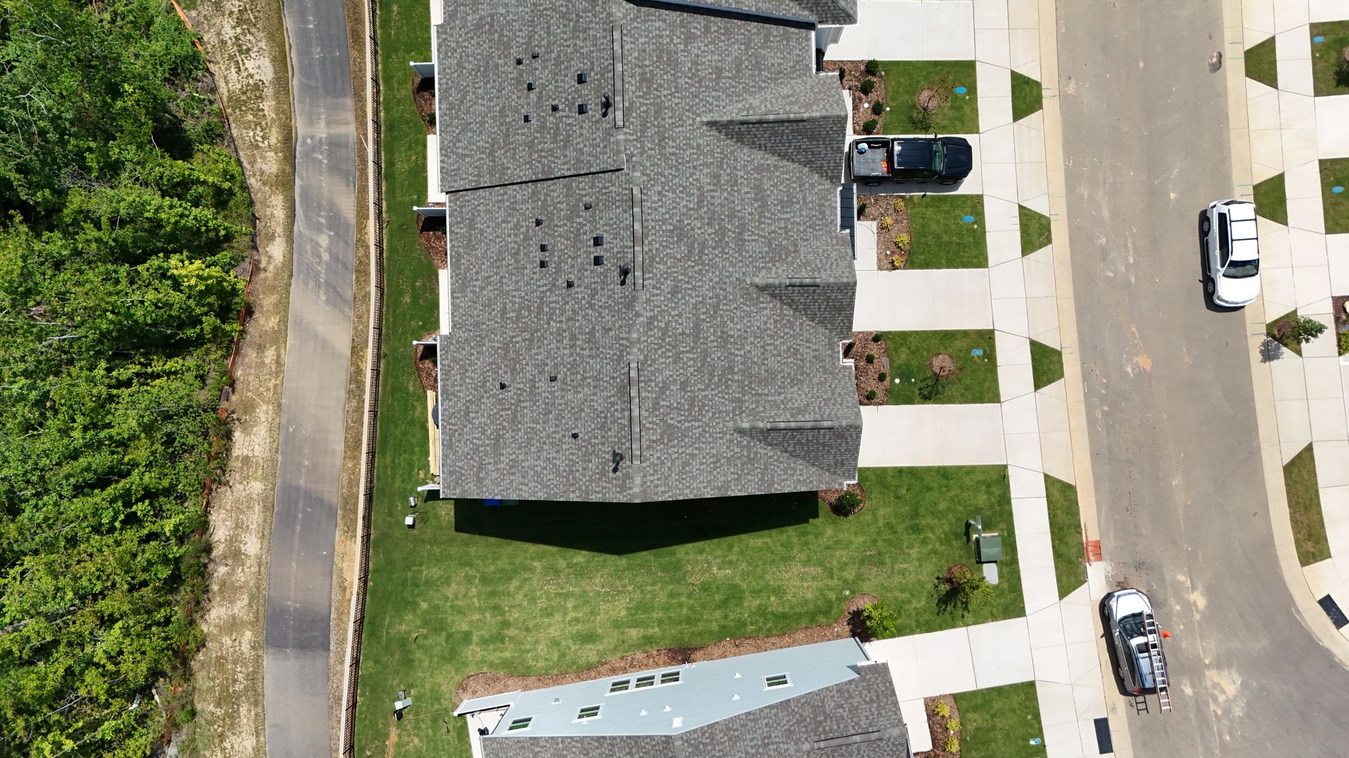 Aerial view of townhomes with gray roofs, green yards, and cars parked on a paved road.
