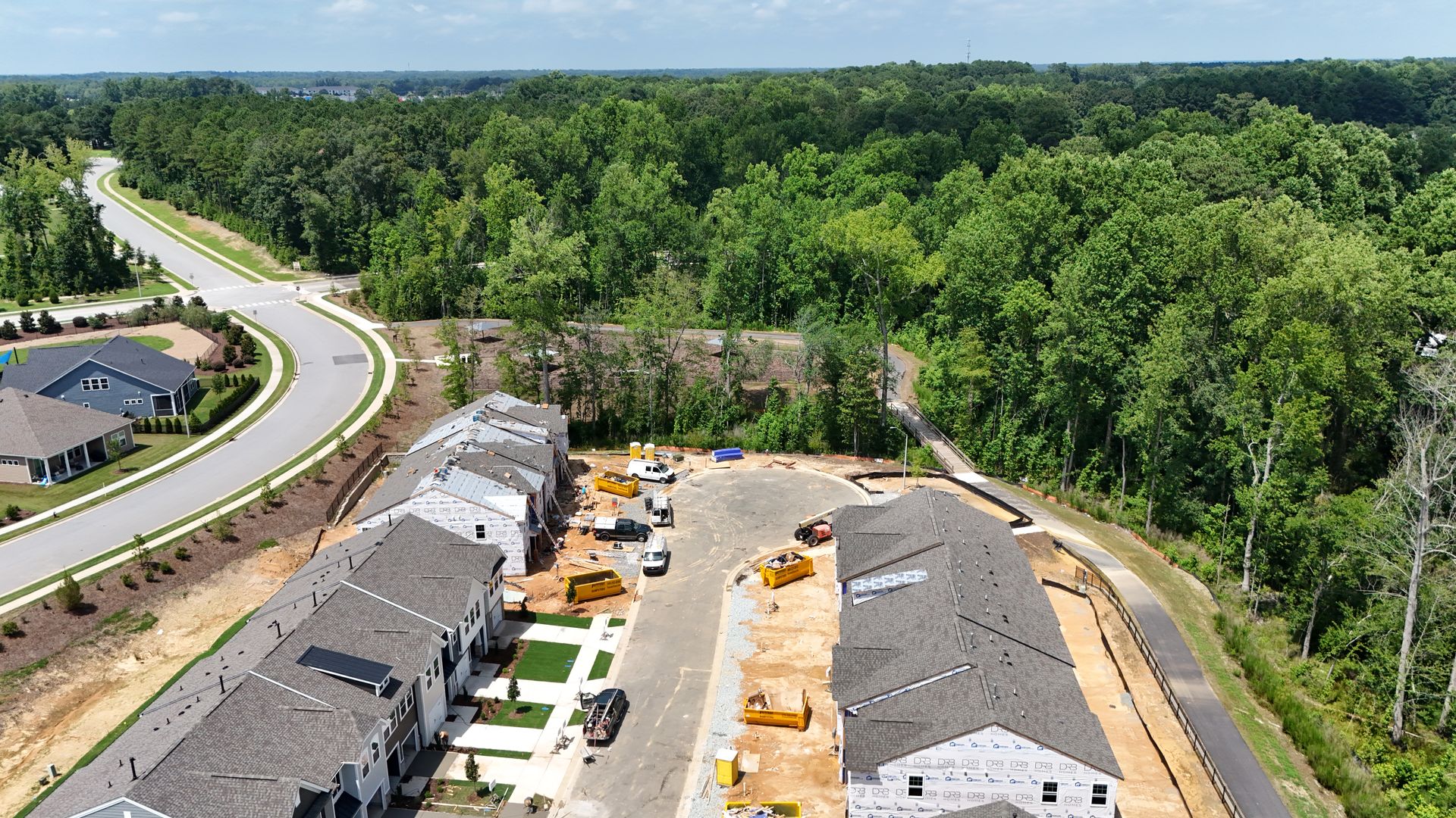 Aerial view of new townhouses under construction next to a wooded area and curved road.