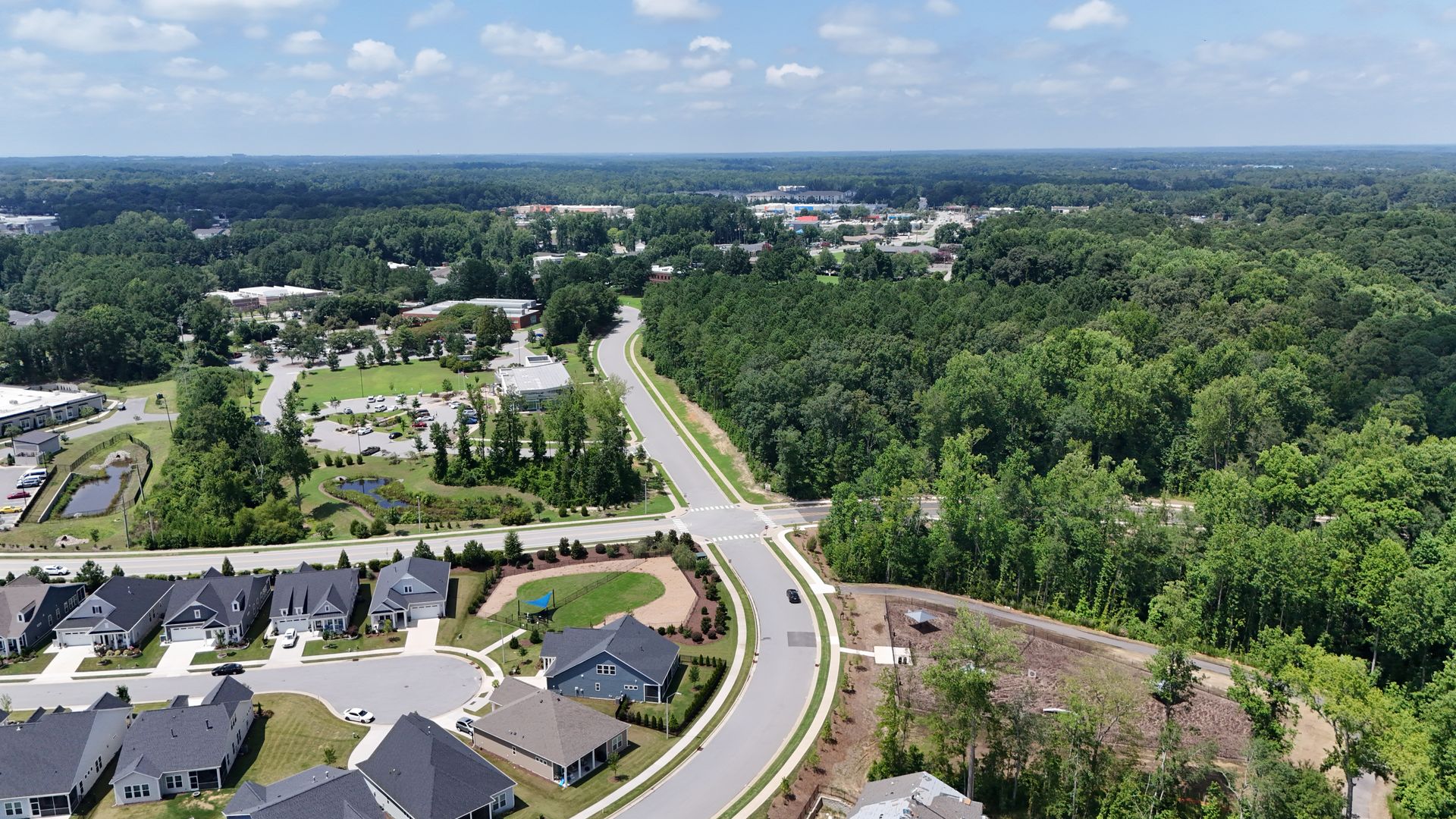 Aerial view of a suburban neighborhood with houses, roads, and a large forest in the background.
