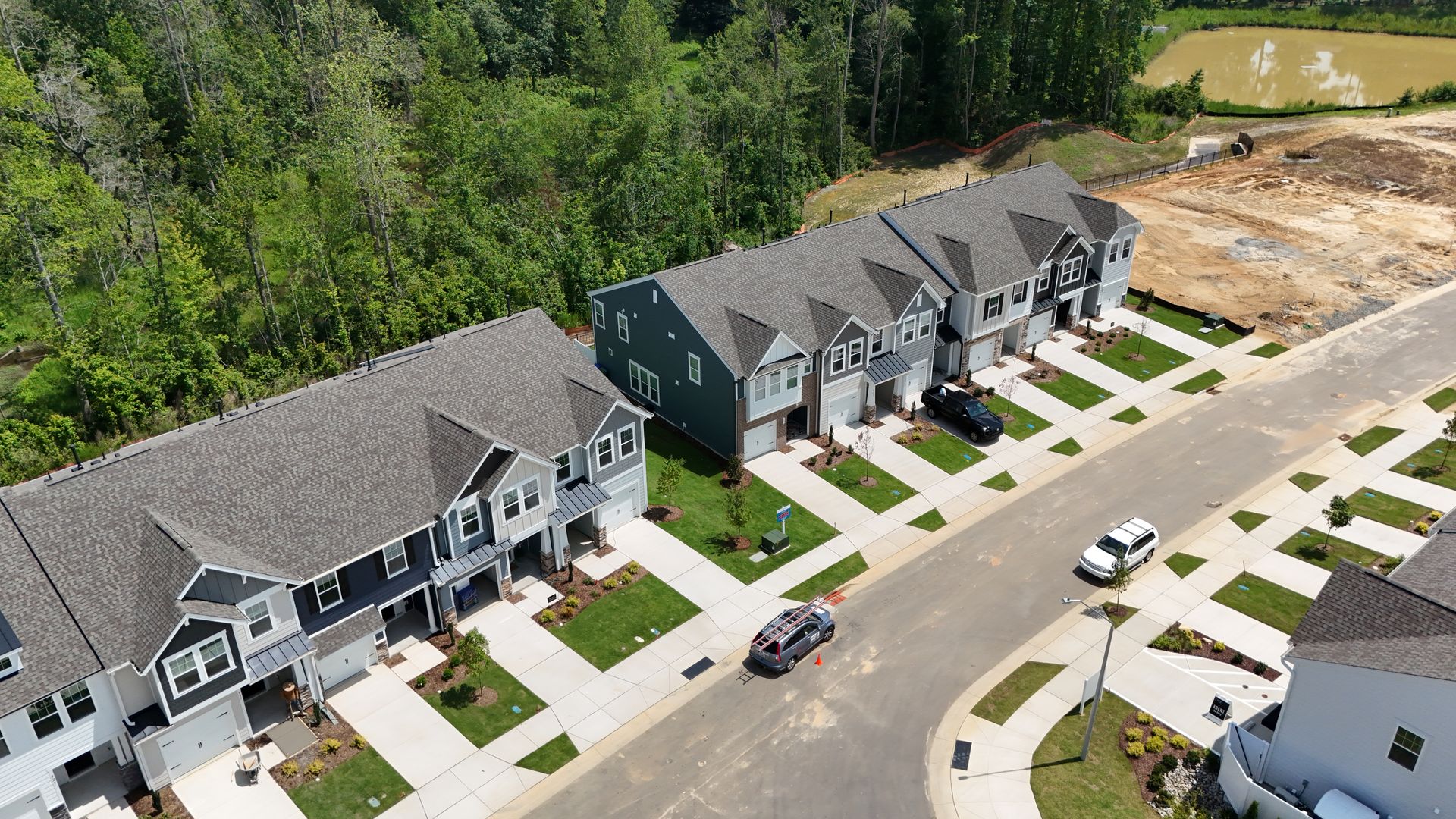 Row of townhouses with cars parked along the street, grass and trees visible.
