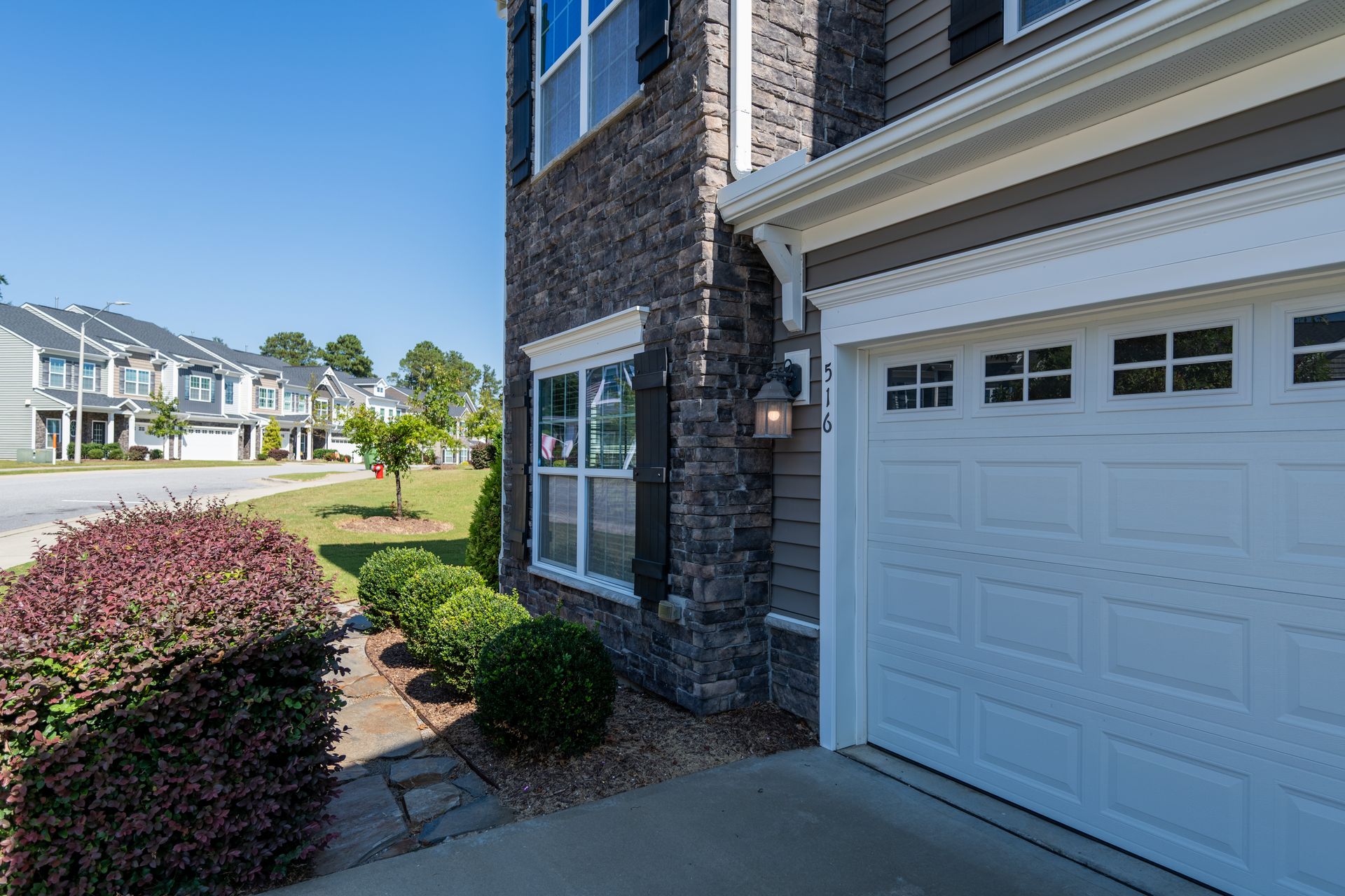 Corner of a two-story house with stone and gray siding, white garage door, and landscaped front yard.