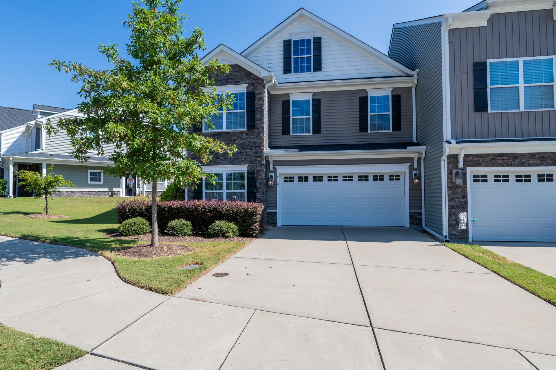 Two-story house with brick facade and gray siding; white garage door. Sunny day.