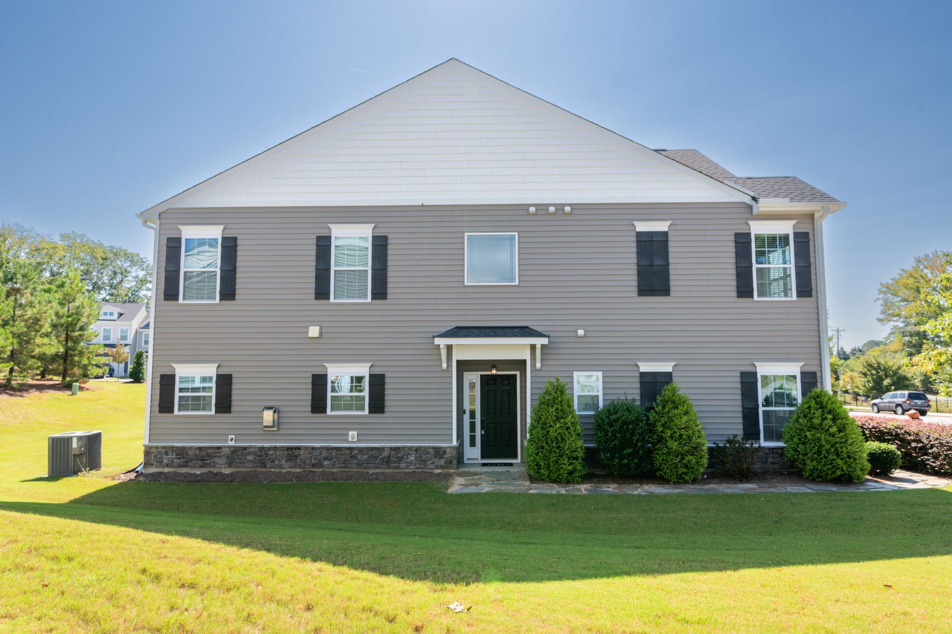 Two-story gray house with black shutters and green lawn under a blue sky.