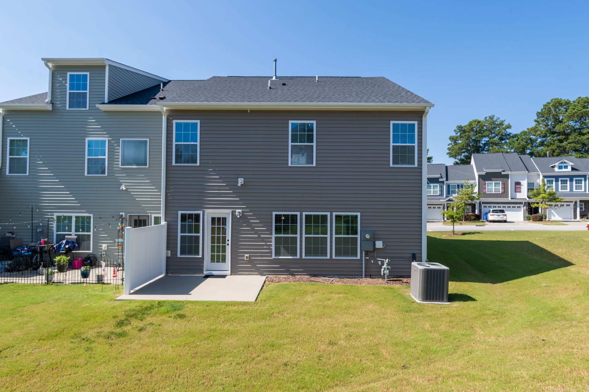 Back of a gray house with a small patio, grassy lawn, and blue sky in a residential neighborhood.
