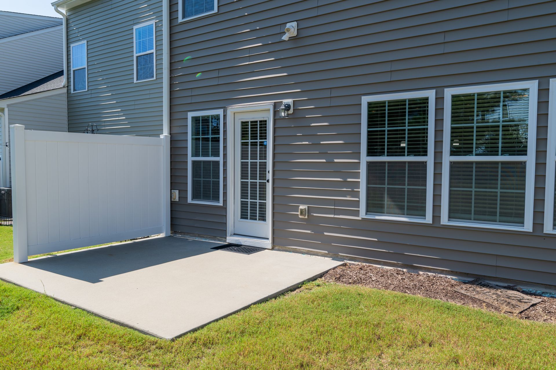 Back patio with door, windows, and white privacy fence; gray siding on a house.