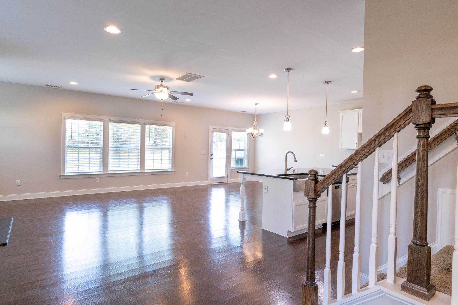Interior of a house with hardwood floors, a kitchen island, and a staircase. Natural light fills the space.