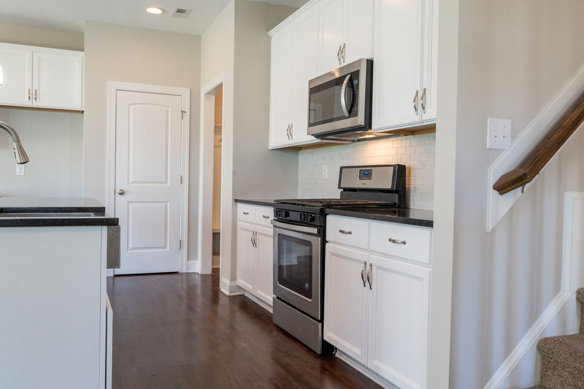 Kitchen with white cabinets, stainless steel appliances, dark countertops, and wood floors.
