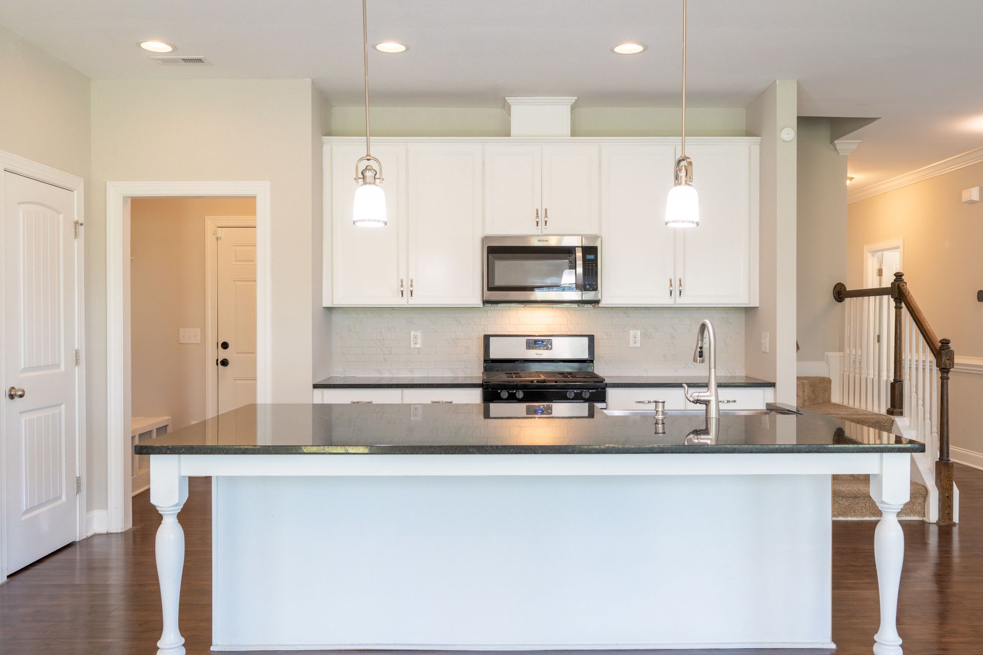 White kitchen with island, stainless steel appliances, and dark countertops.