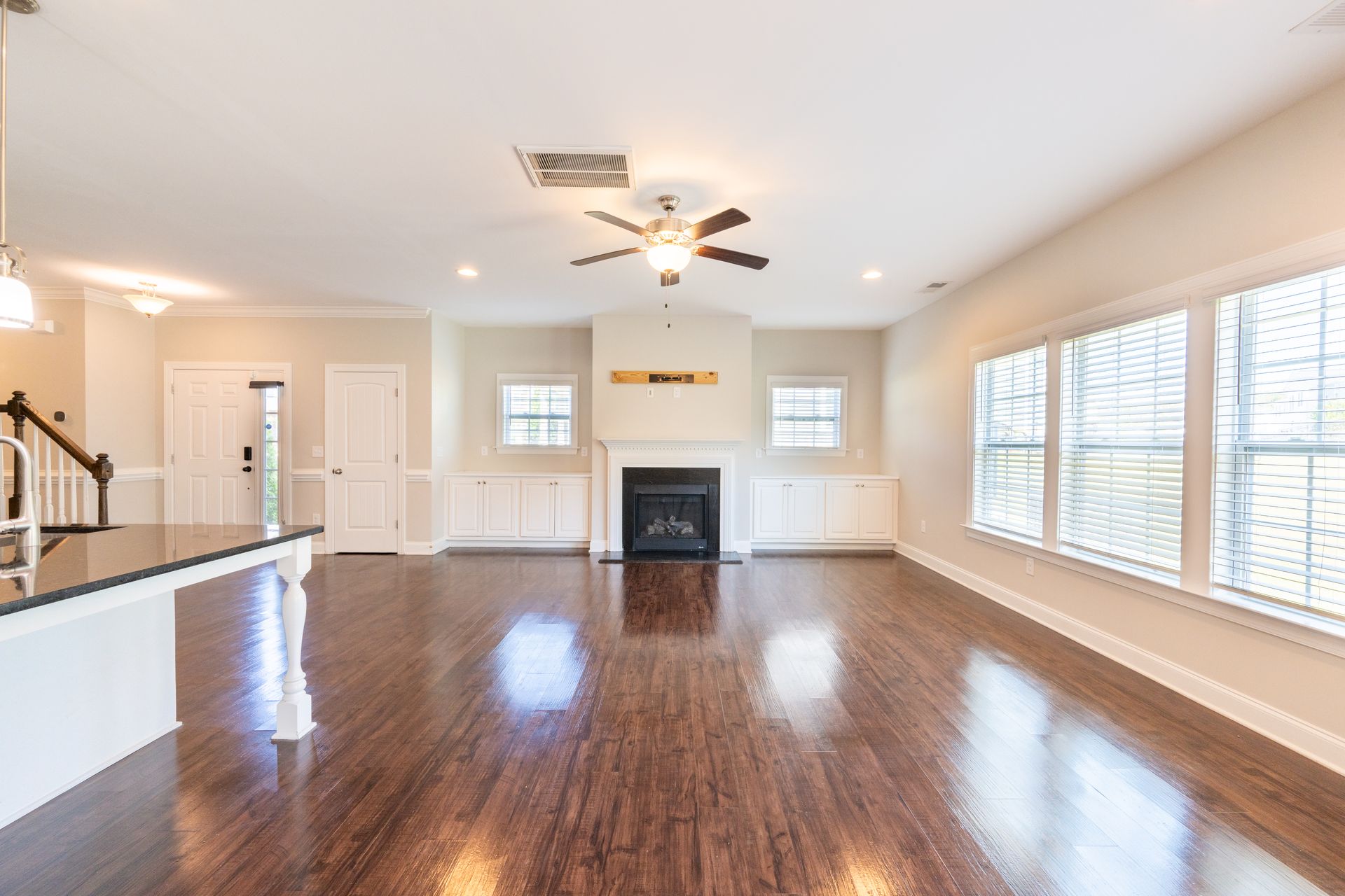 Living room with fireplace, hardwood floors, windows, and ceiling fan.