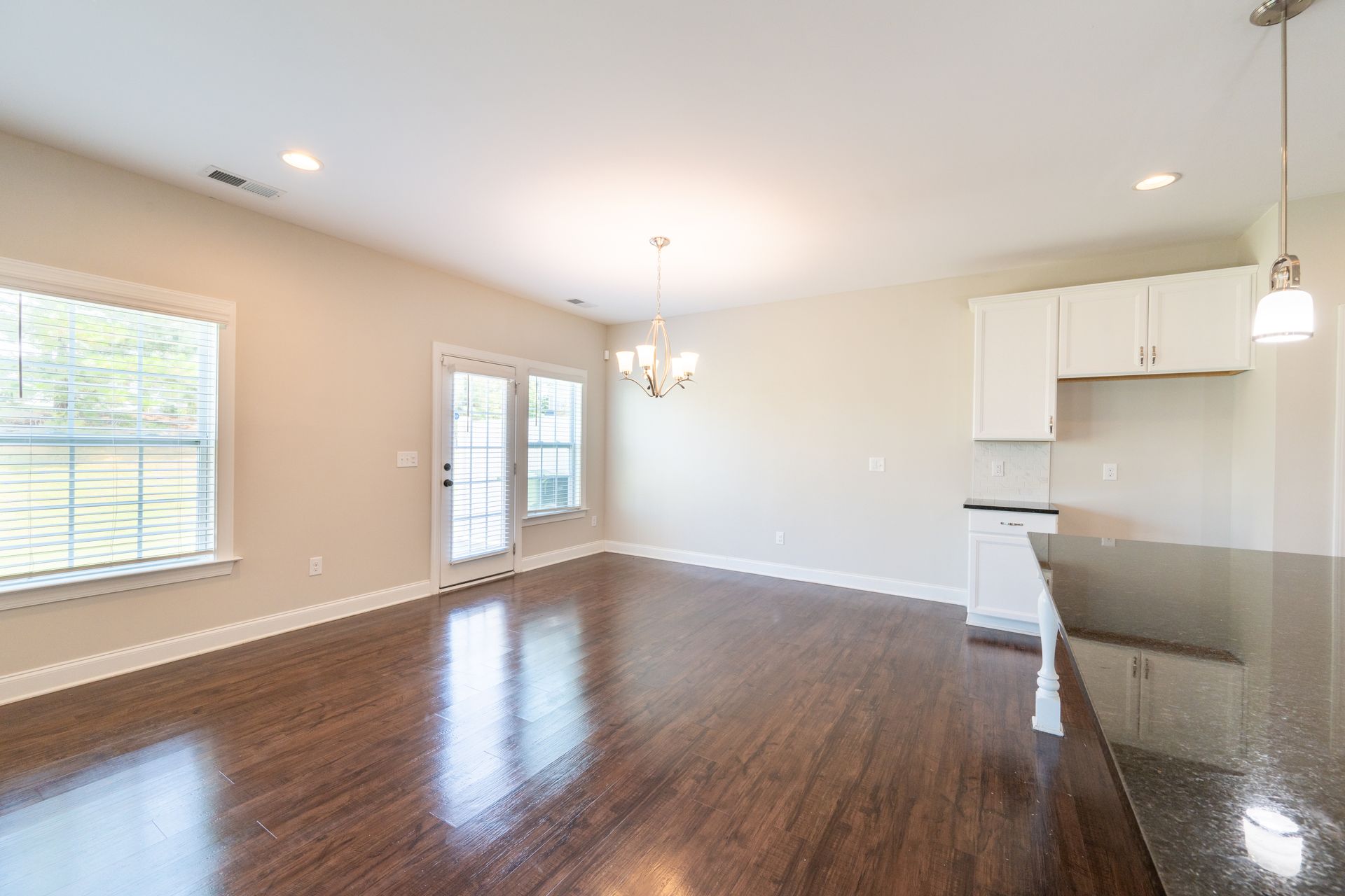Open-concept dining/kitchen area with dark wood floors, white cabinets, and French doors.