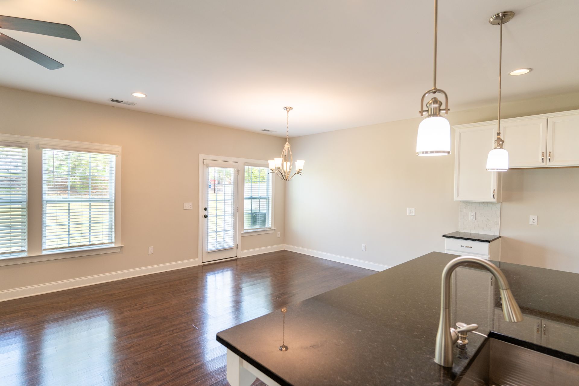 Open-plan kitchen with dark counter, white cabinets, and hardwood floor. Sunlight streams through windows and French doors.