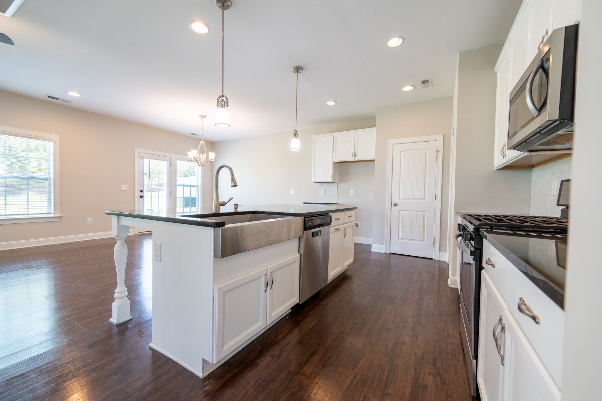 Bright kitchen with island, white cabinets, stainless steel appliances, dark countertops, and hardwood floors.