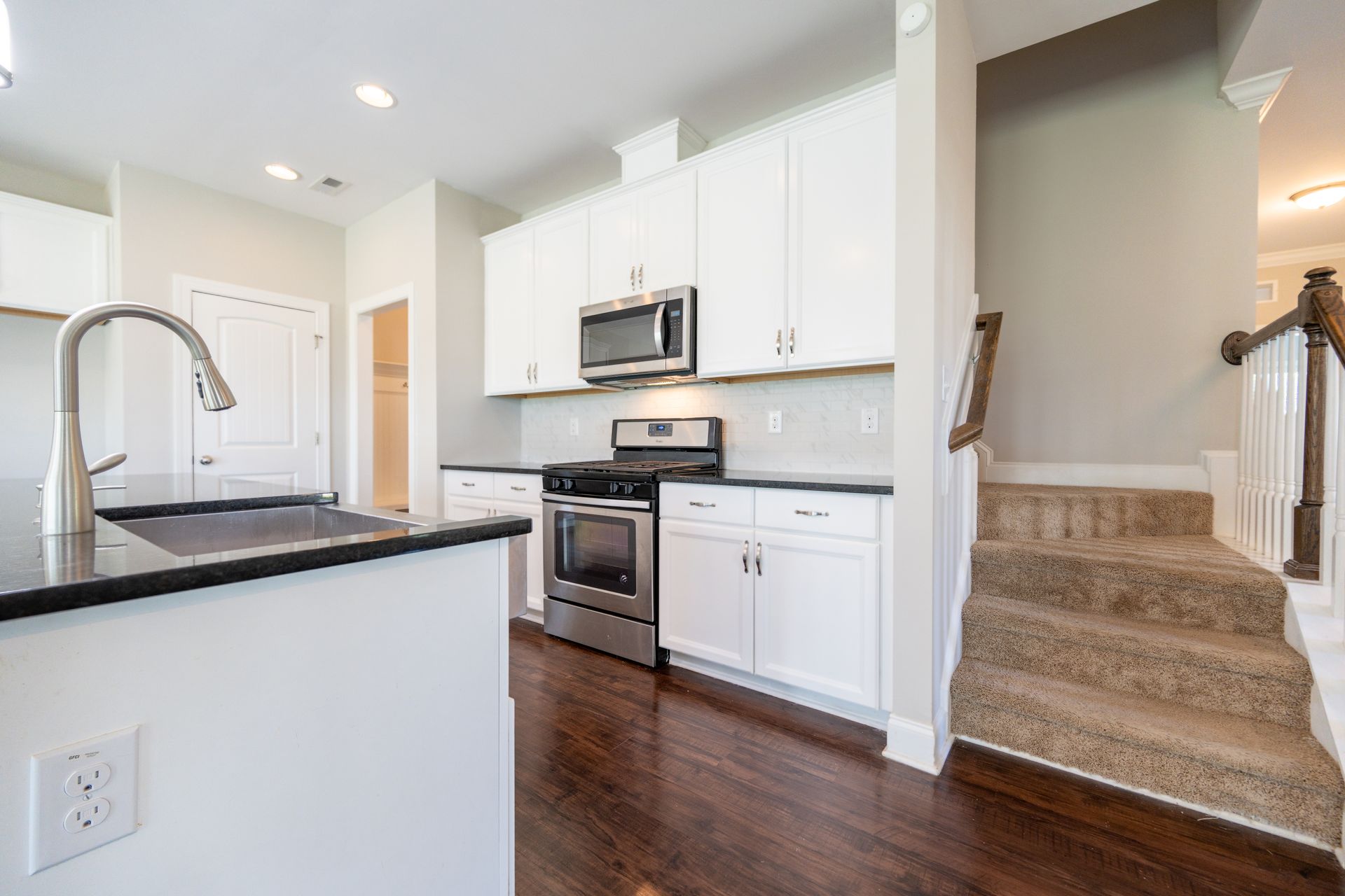 White kitchen with dark countertops, stainless steel appliances, and a staircase.