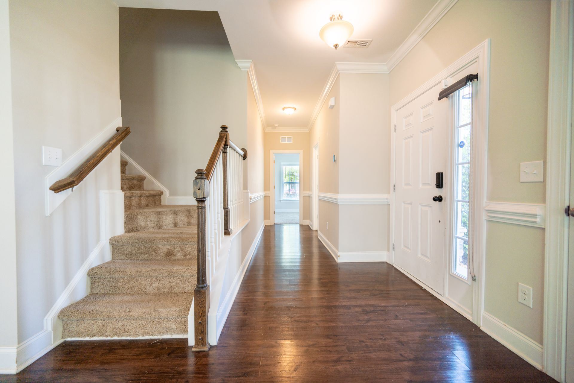 Entryway with stairs on the left, dark wood floors, light-colored walls, and front door on the right.