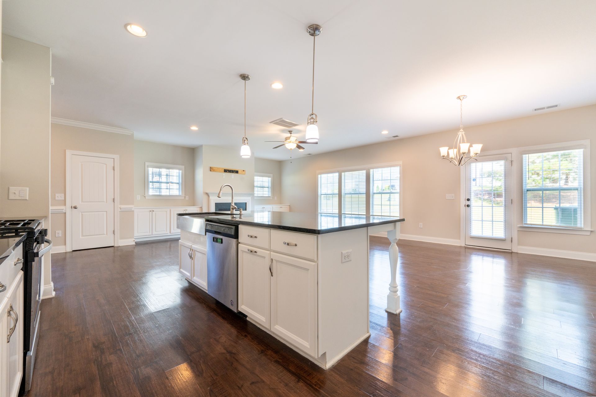Open-plan kitchen with a dark wood floor, white cabinets, black countertop island, and natural light.