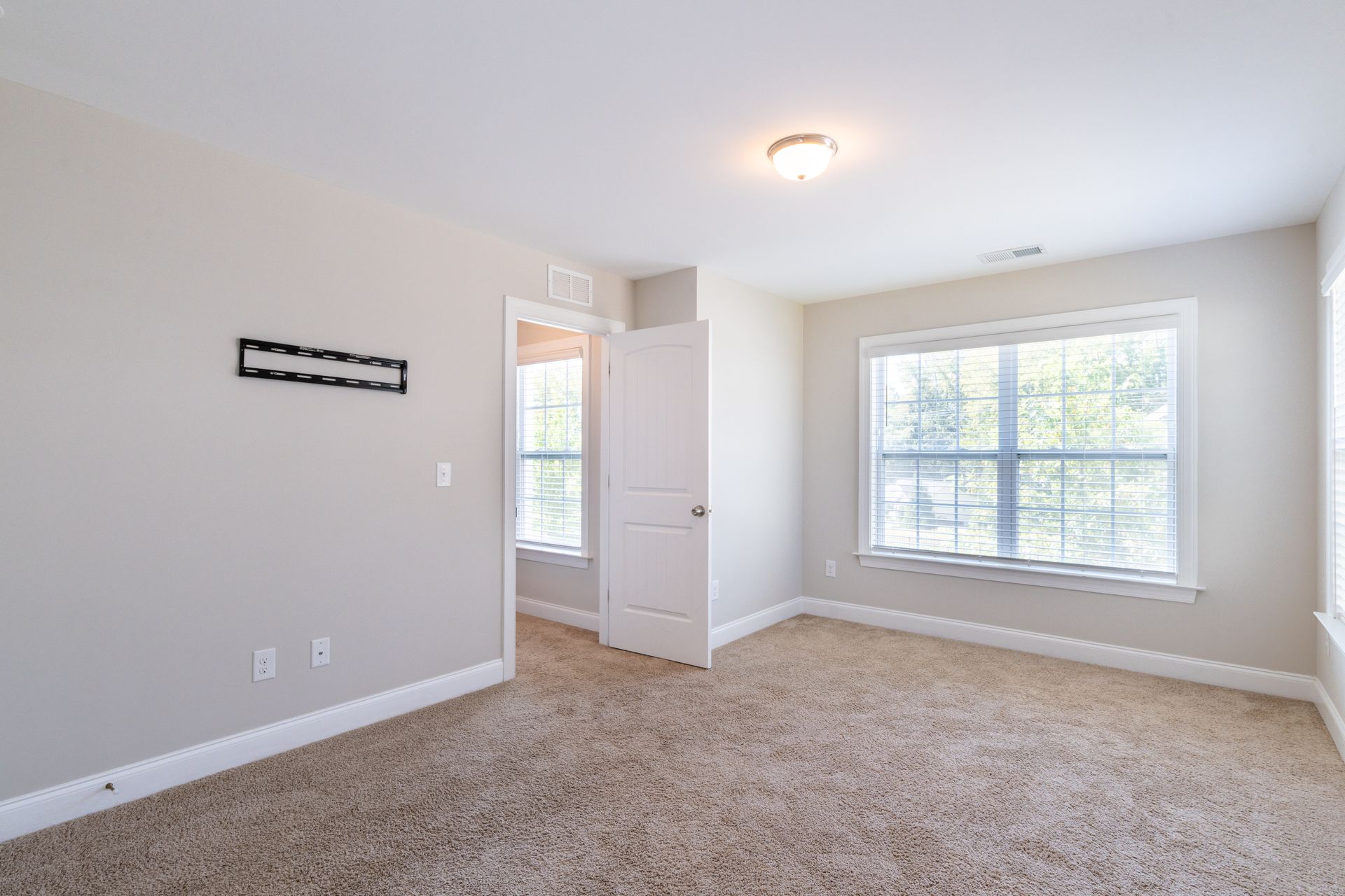 Empty bedroom with beige carpet, light-colored walls, windows, and a doorway.