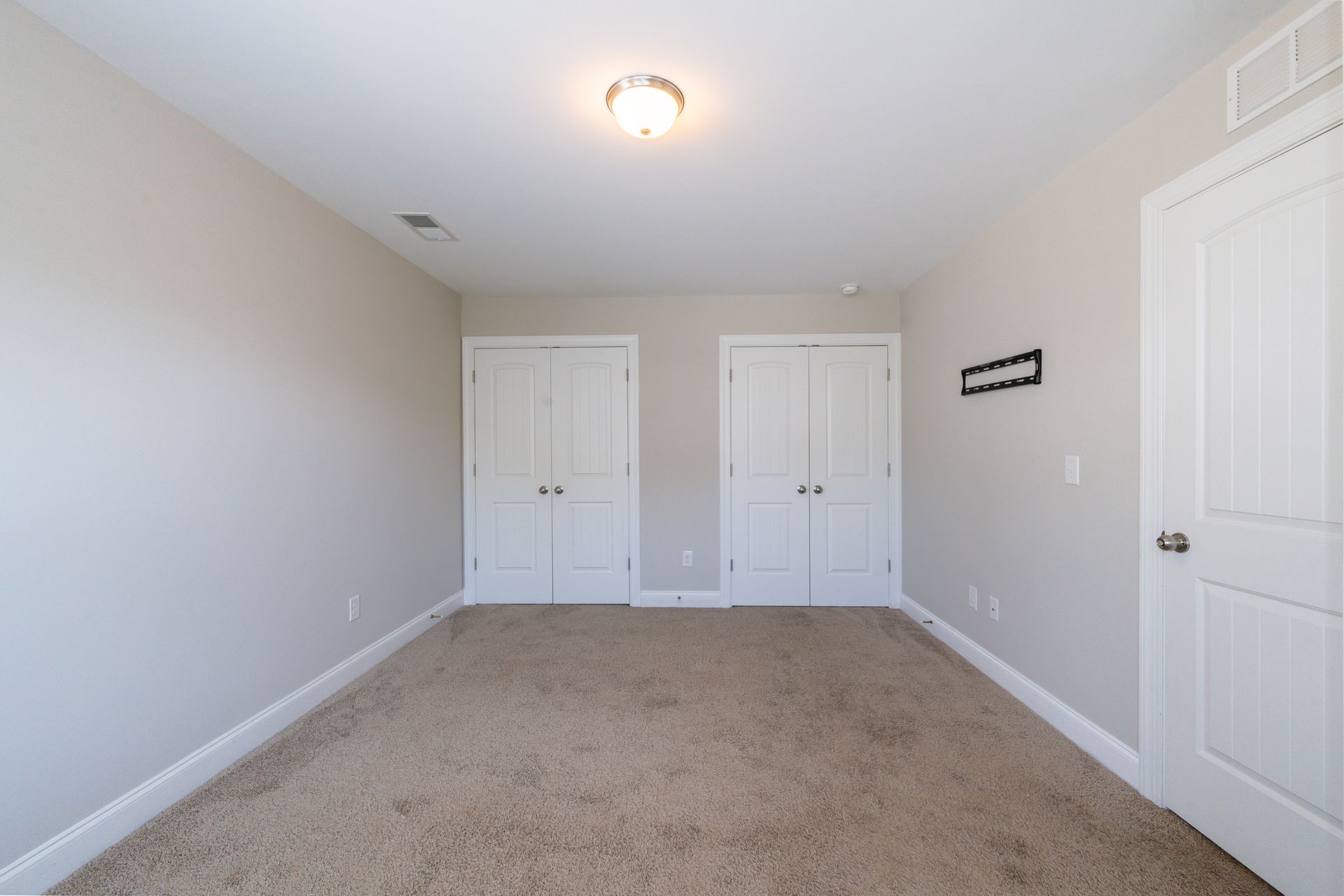 Empty bedroom with beige walls, carpet, three white doors, and ceiling light.