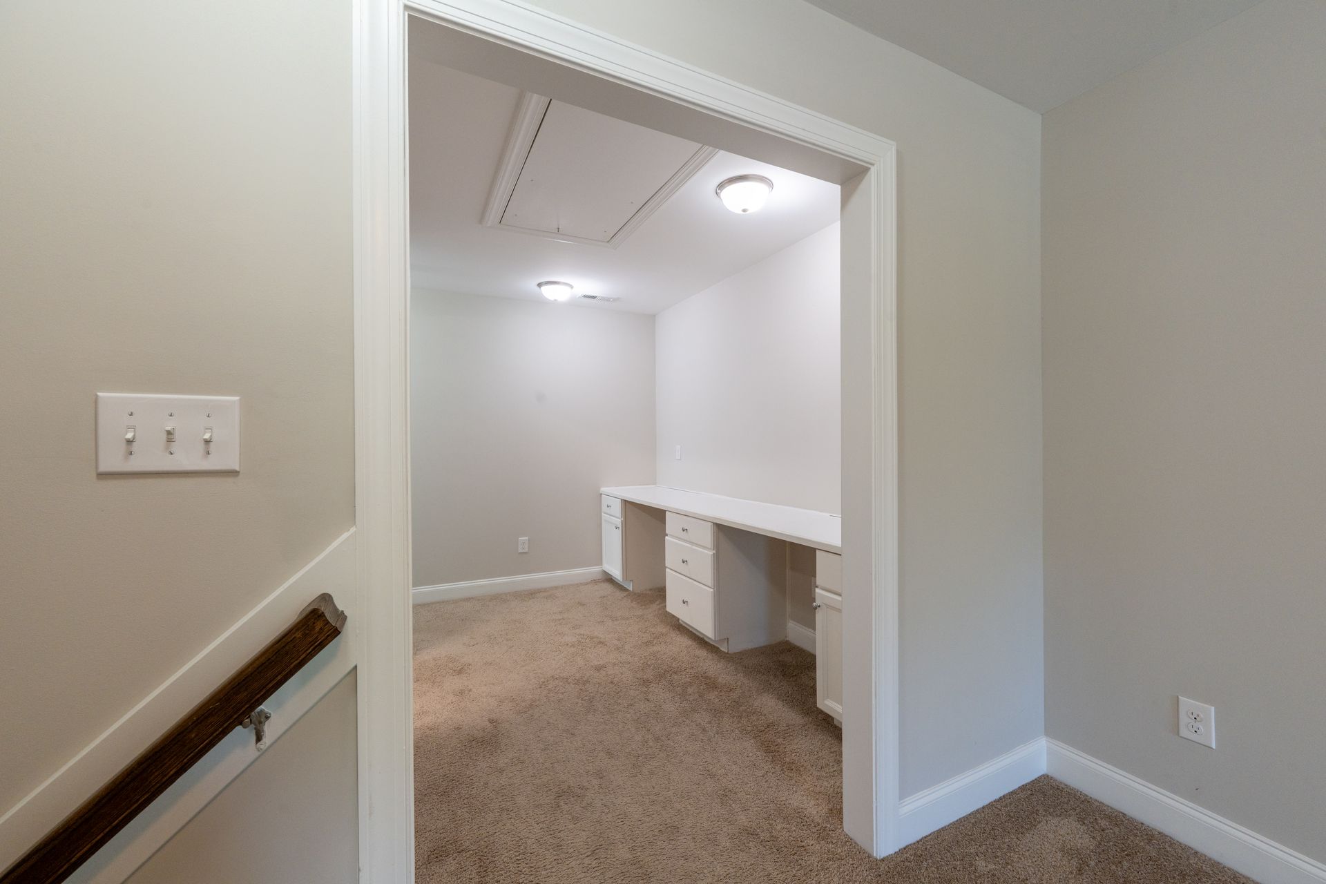 A doorway leads into a small office with white walls, built-in desk, carpet, and overhead lighting.