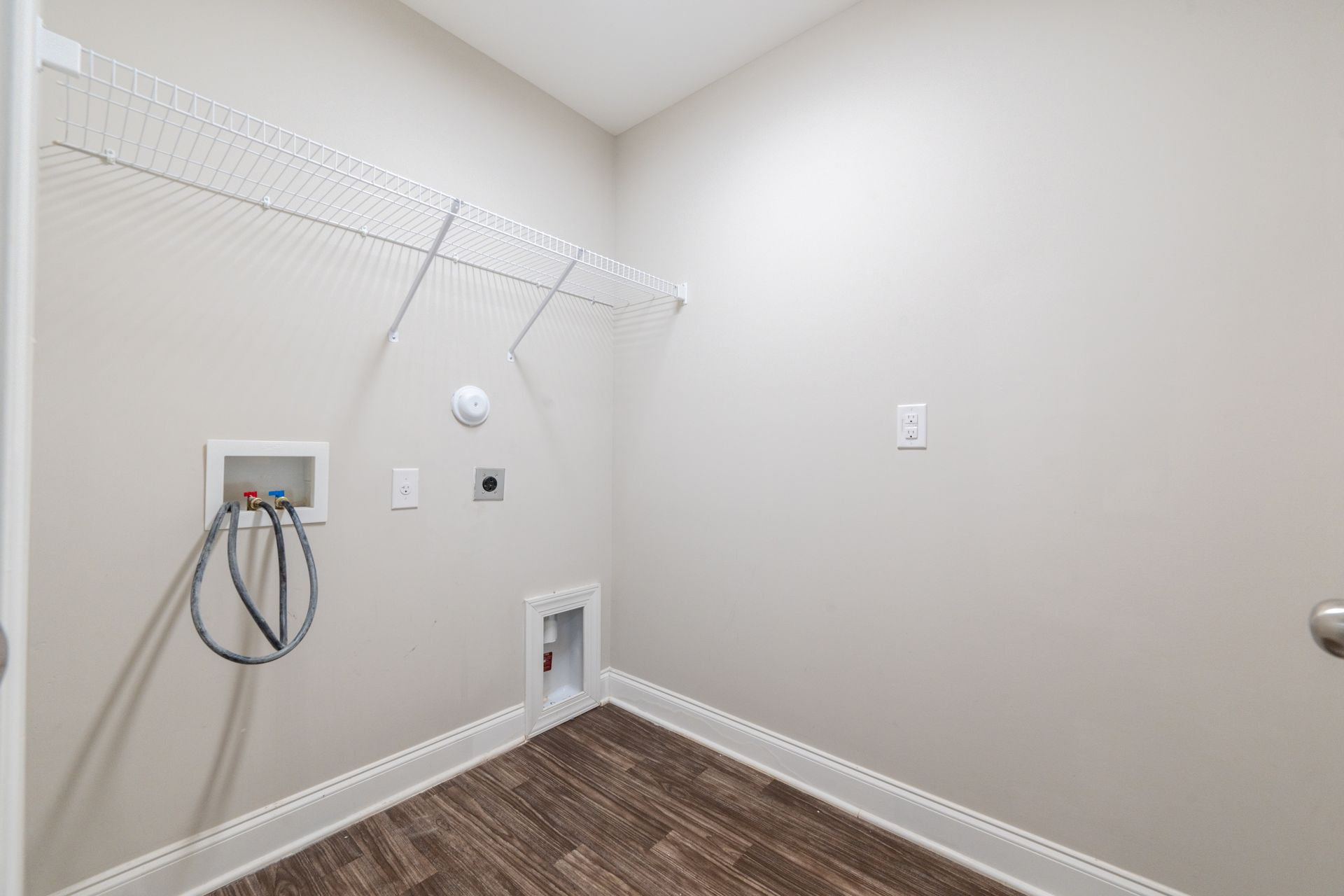 Laundry room with a wire shelf, water hookups, and wood-look flooring.