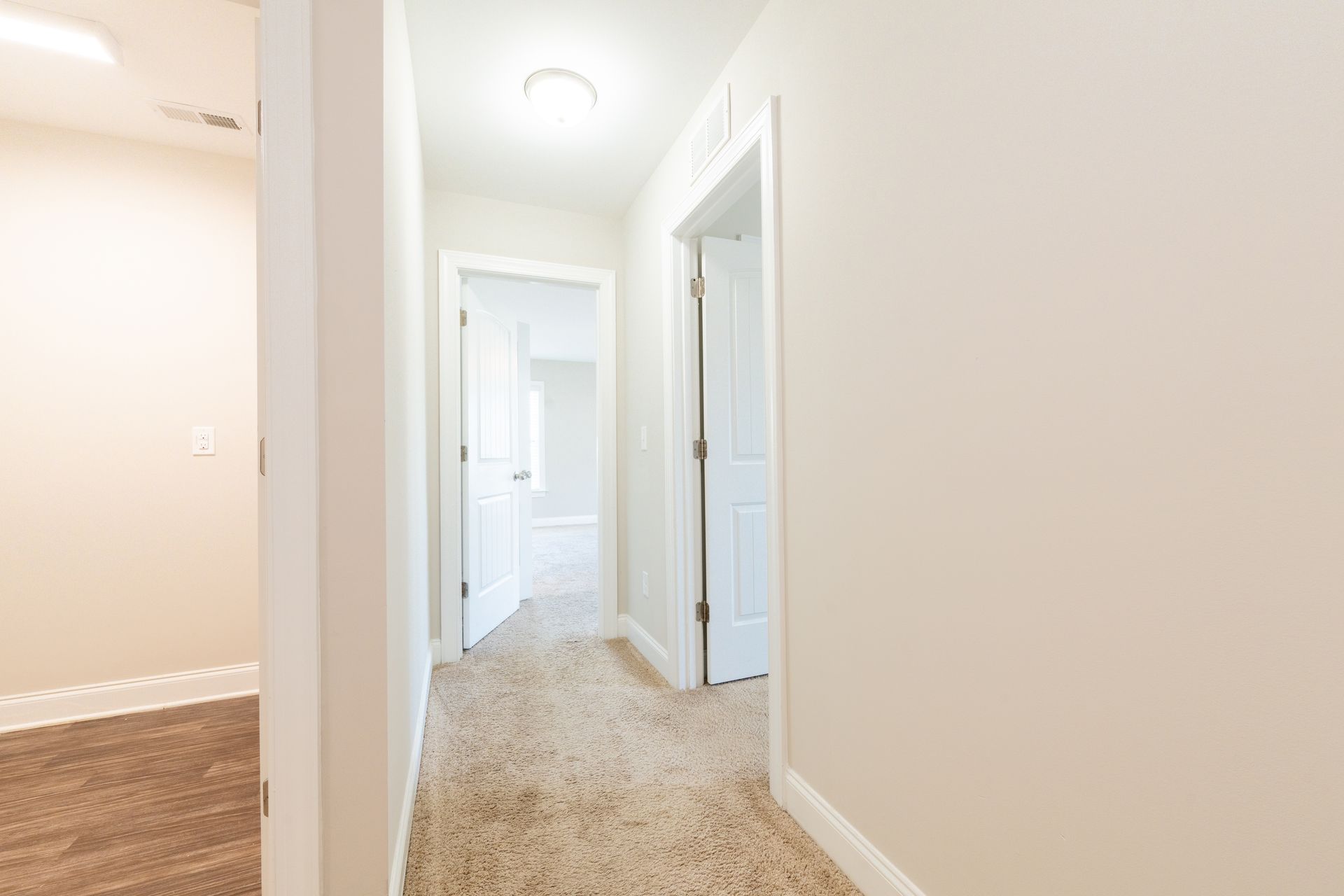 A narrow hallway with beige carpet and white doors.