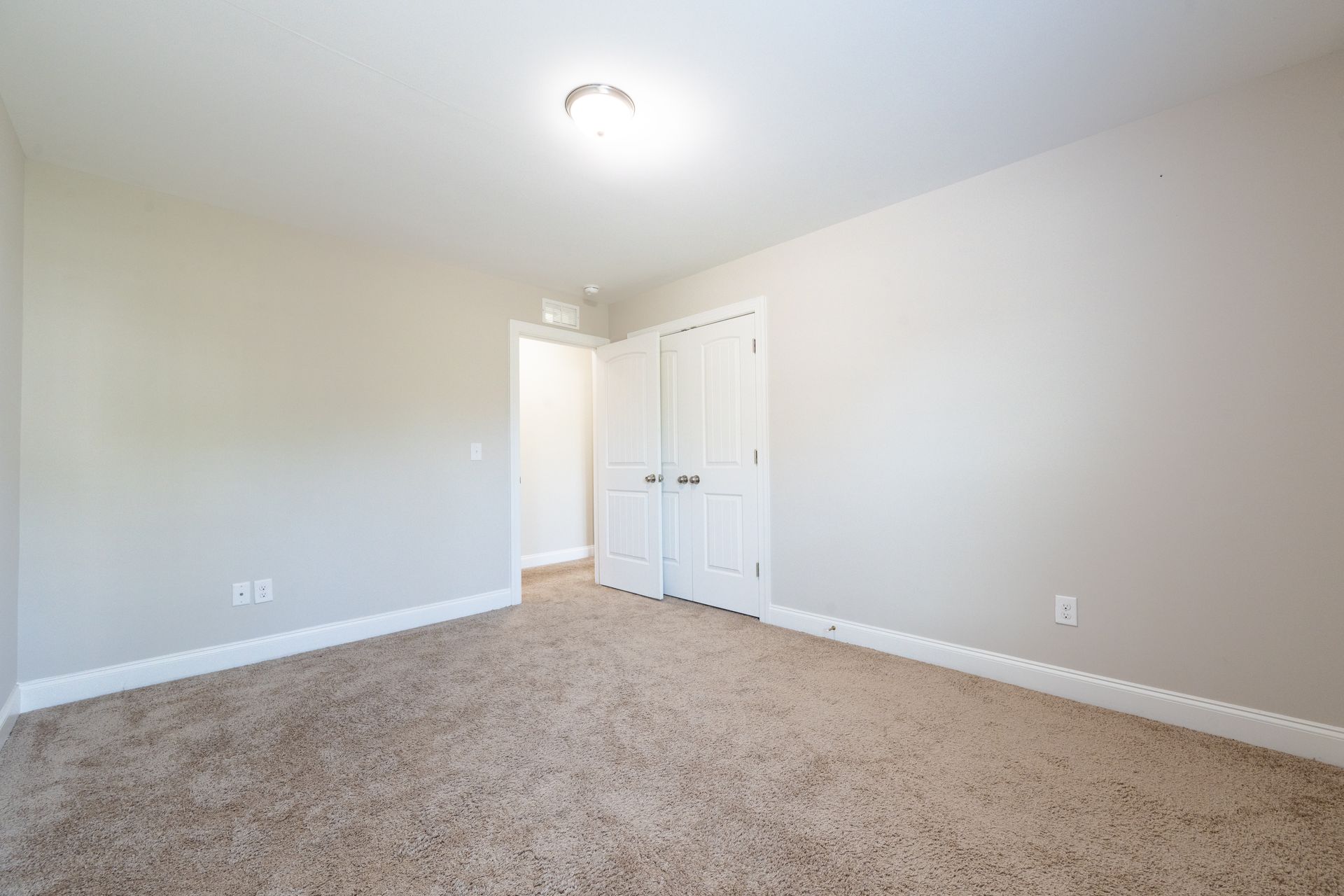 Empty bedroom with beige carpet, white walls, and closed white doors.