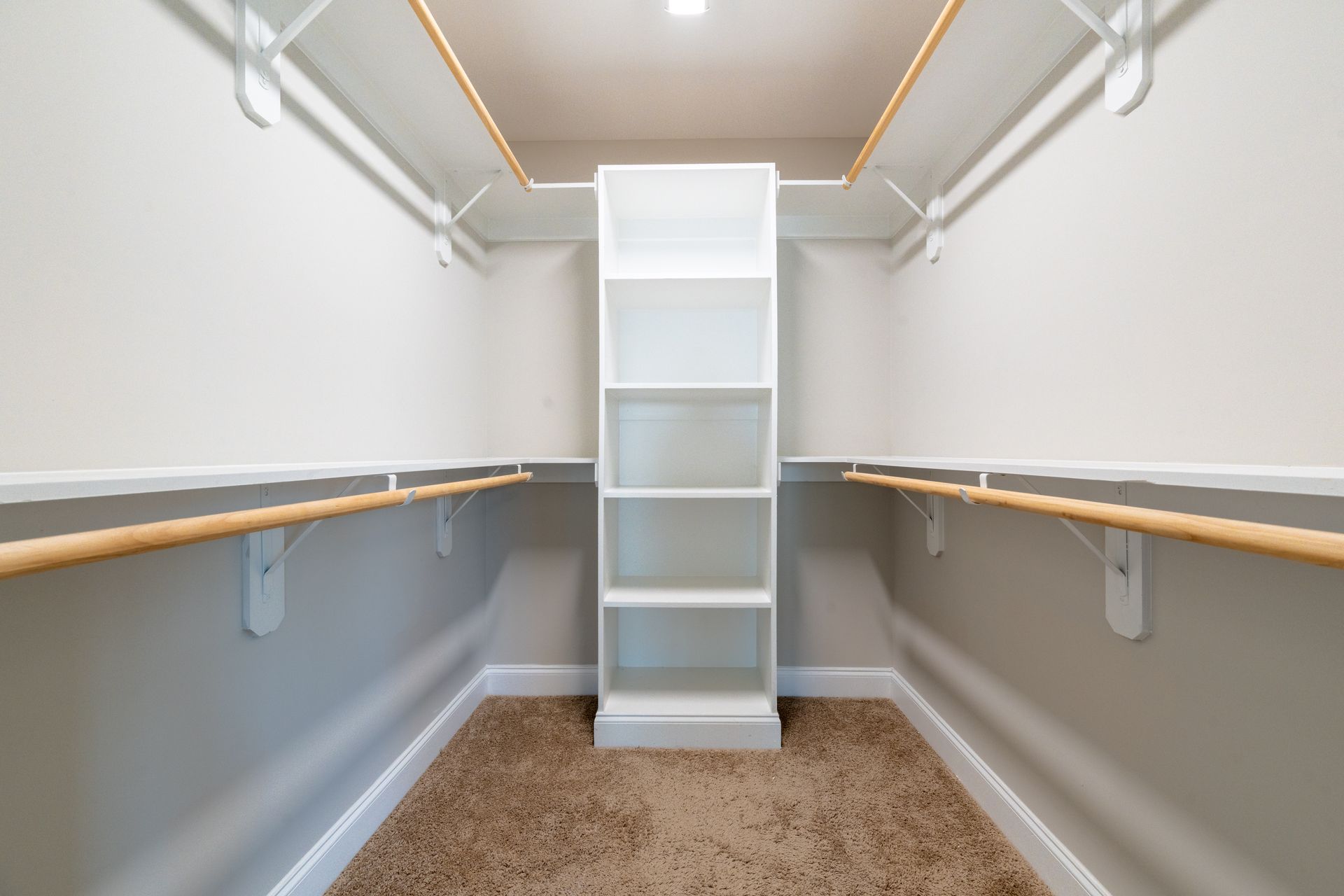 Empty, organized walk-in closet with shelving and hanging rods; beige walls, carpet, and shelves.
