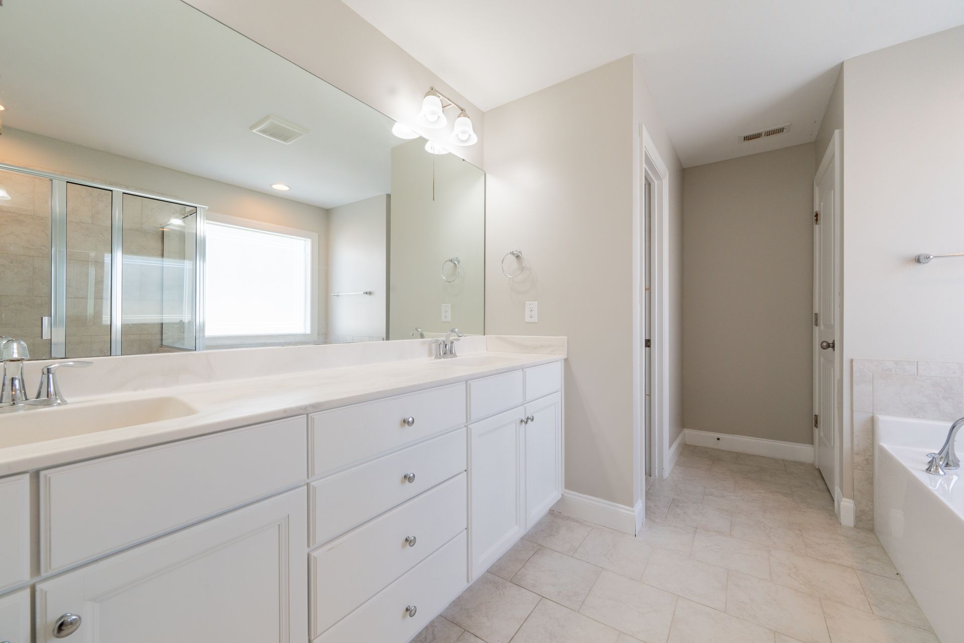 Spacious white bathroom with a double vanity, large mirror, and a door leading to another room.