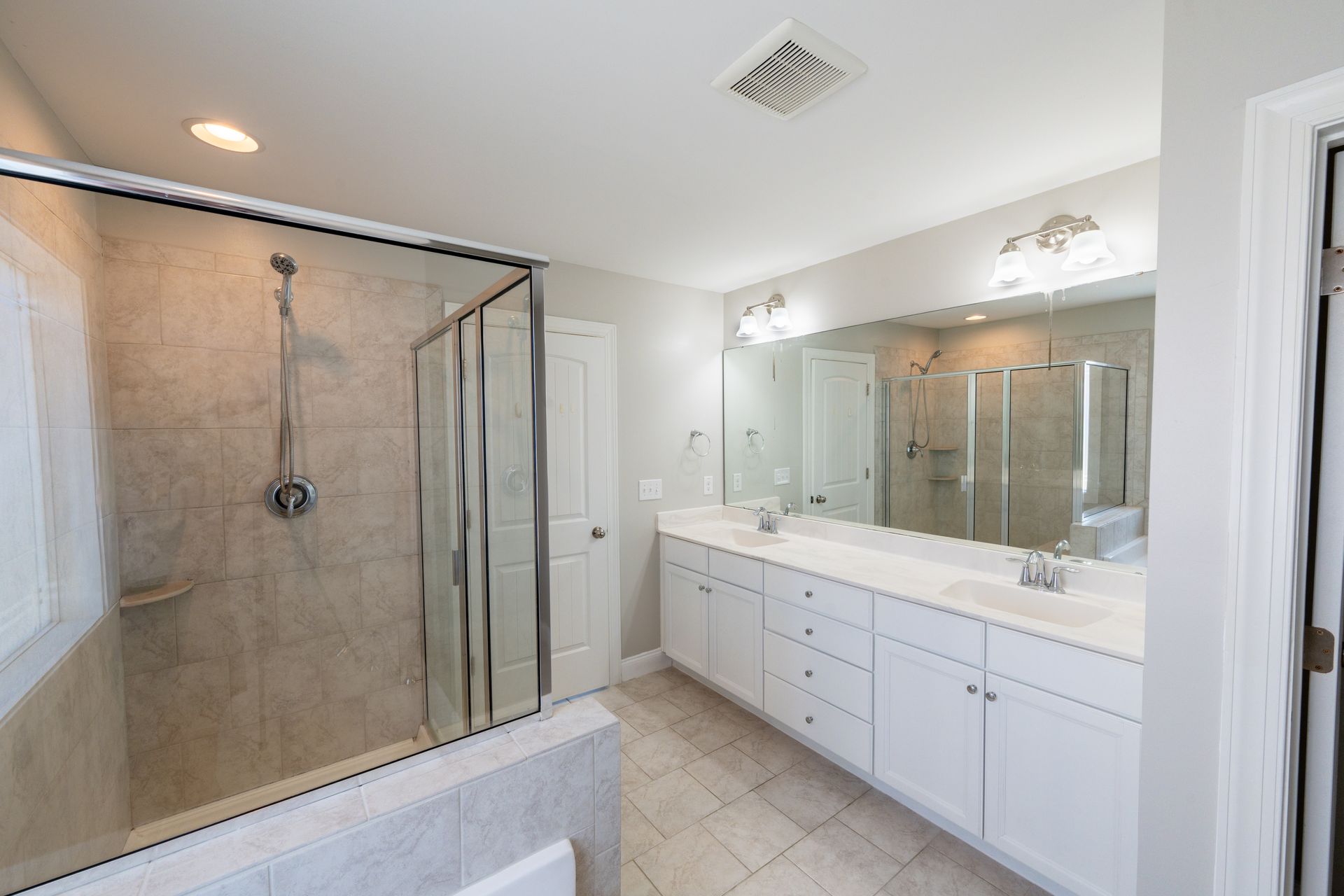 Spacious bathroom with a glass-enclosed shower, white vanity, and large mirror.
