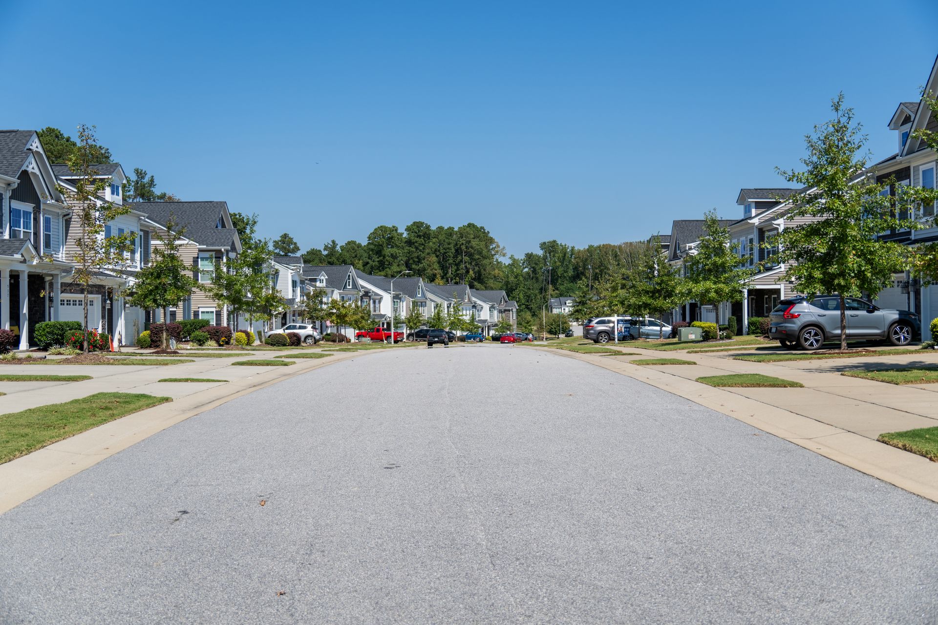 A suburban street lined with houses and cars under a clear blue sky.