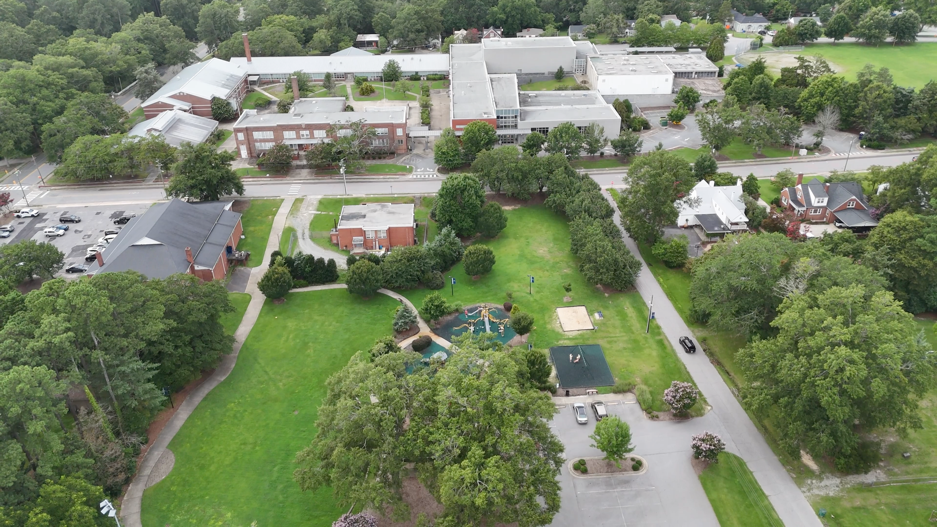 Aerial view of a school with buildings, trees, a playground, and a parking lot.