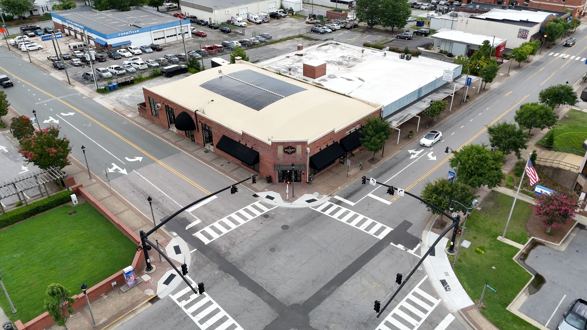 Aerial view of an intersection with a brick building at the corner, crosswalks, and cars on the road.