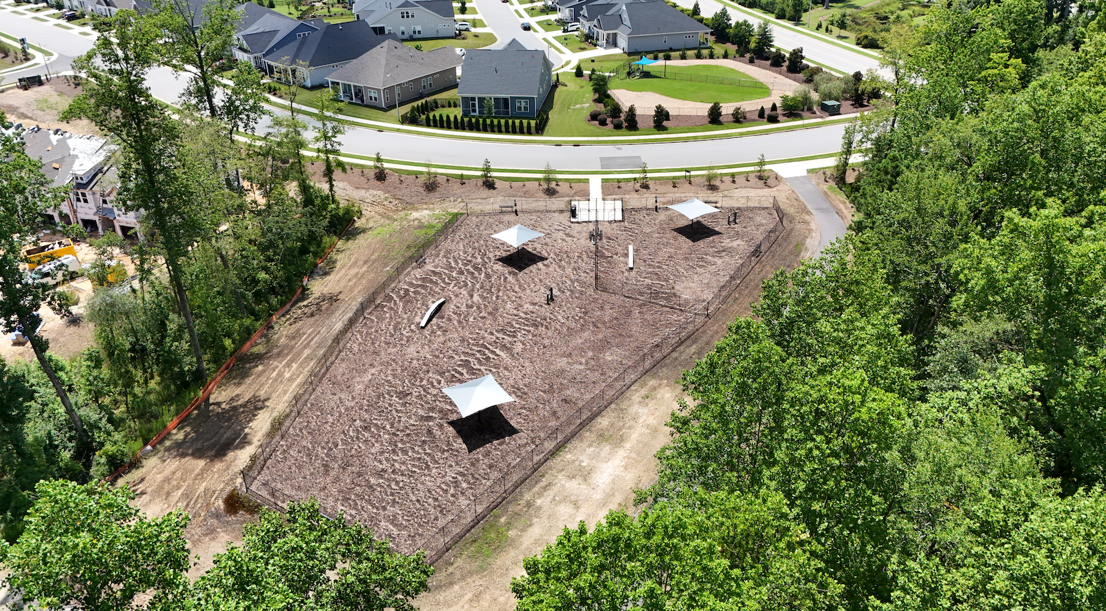 Aerial view of a park with three shade structures, path, and mulch, surrounded by trees and residential area.