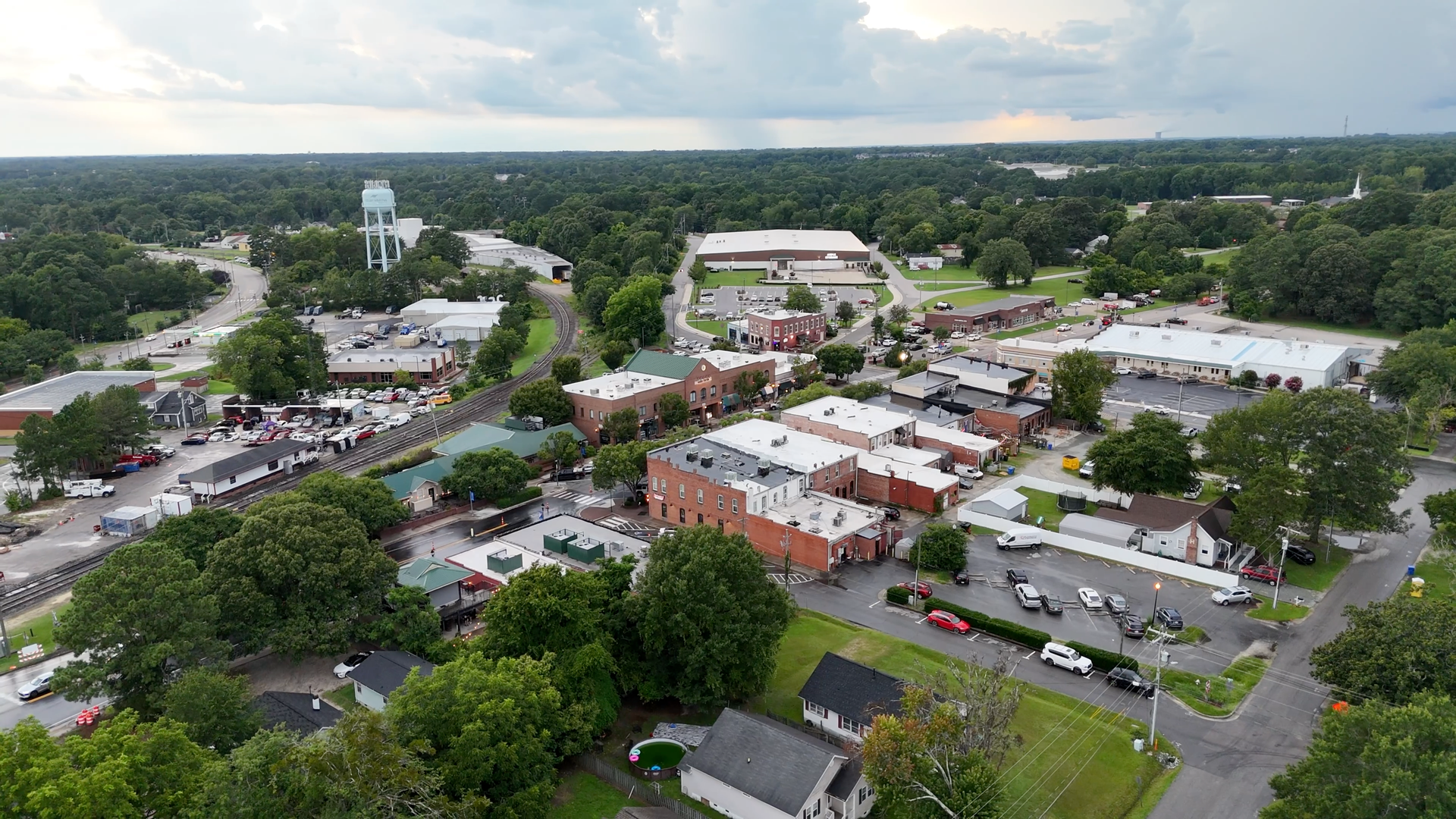 Aerial view of a small town with brick buildings and a water tower surrounded by trees under a cloudy sky.