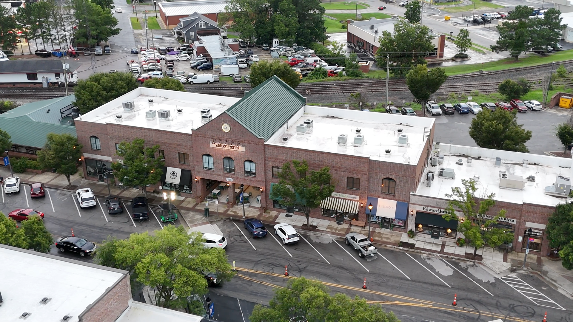 Buildings with parking and cars, a green-roofed structure prominent, urban setting, cloudy sky.