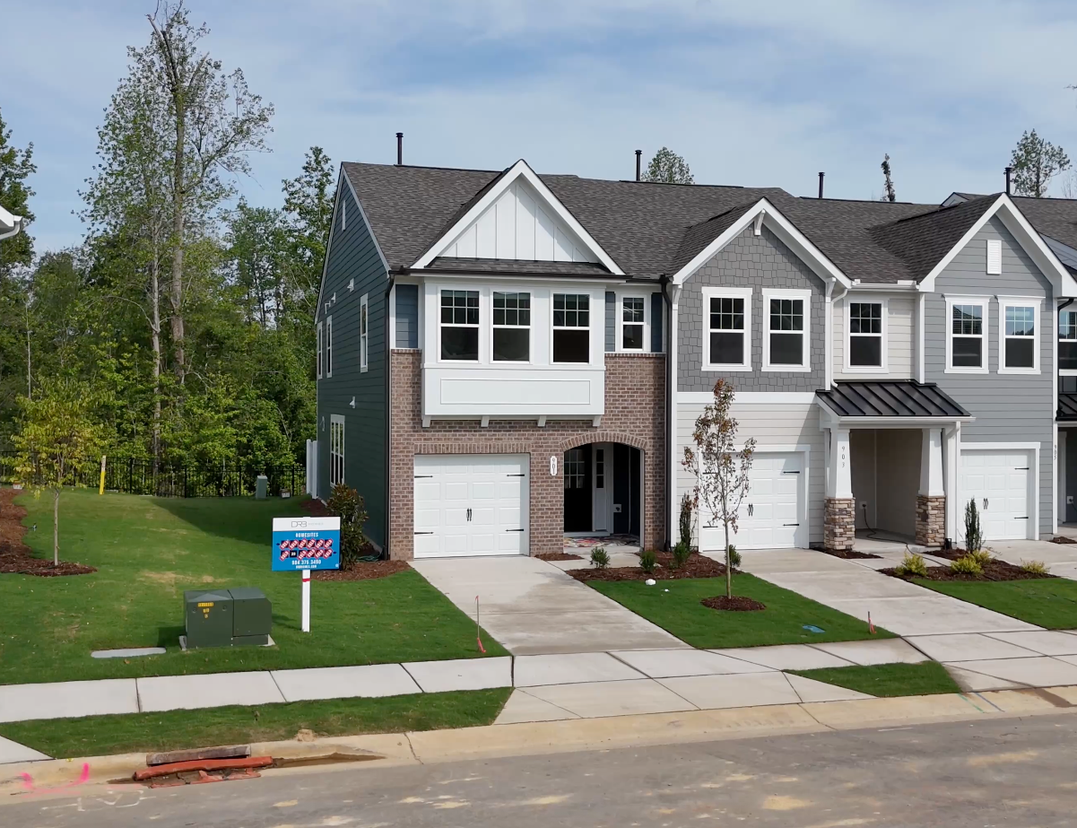 Row of modern townhouses, brick and gray exteriors, green lawn, blue sky.