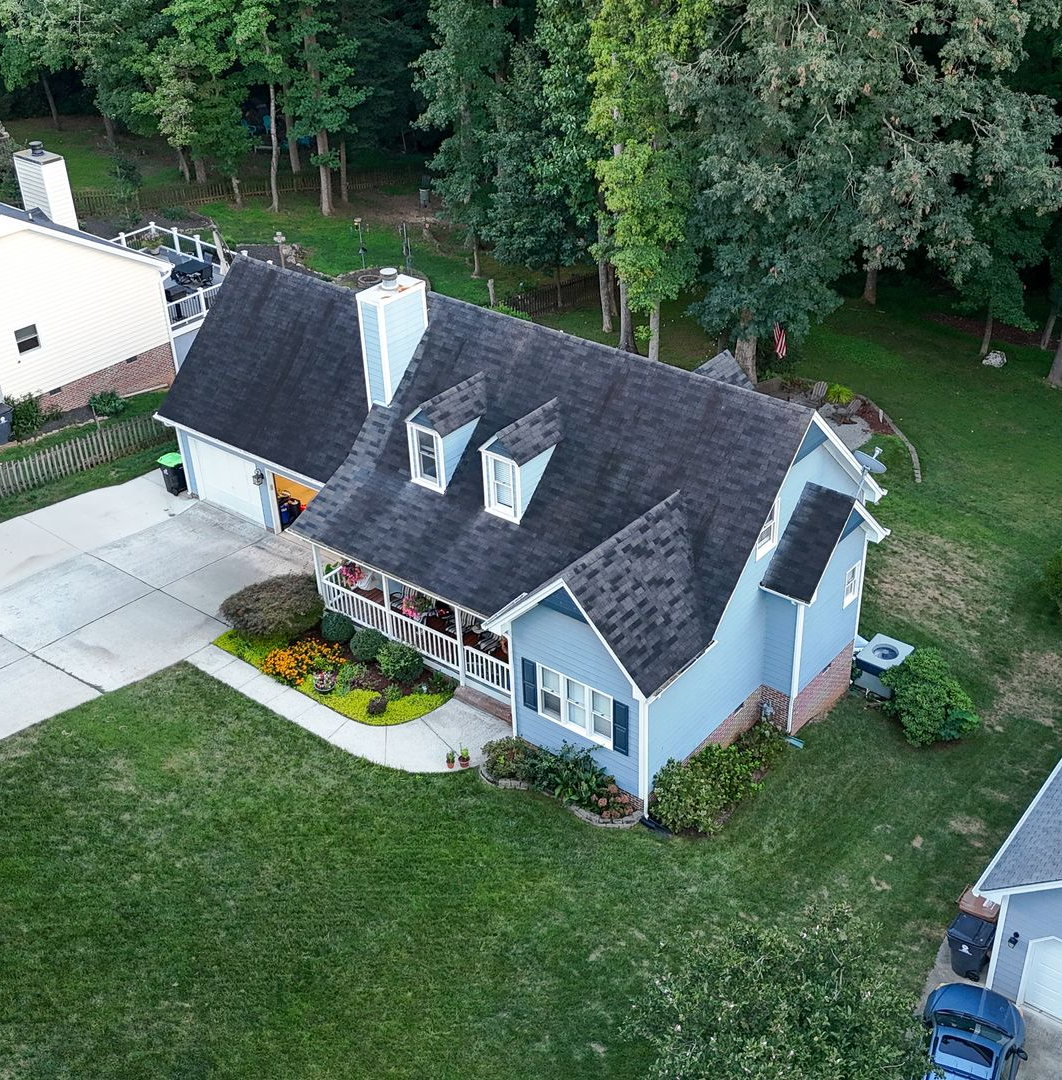 Blue house with a black roof and white trim, green lawn, and trees.