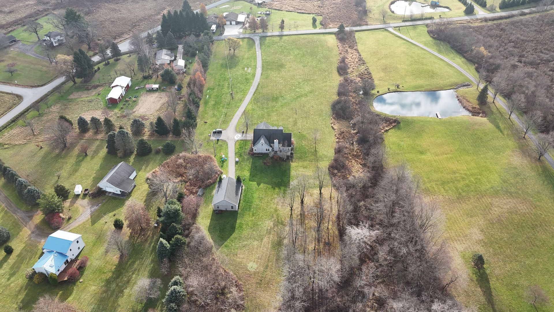 Aerial view of a house and surrounding property with a pond, fields, and some trees.