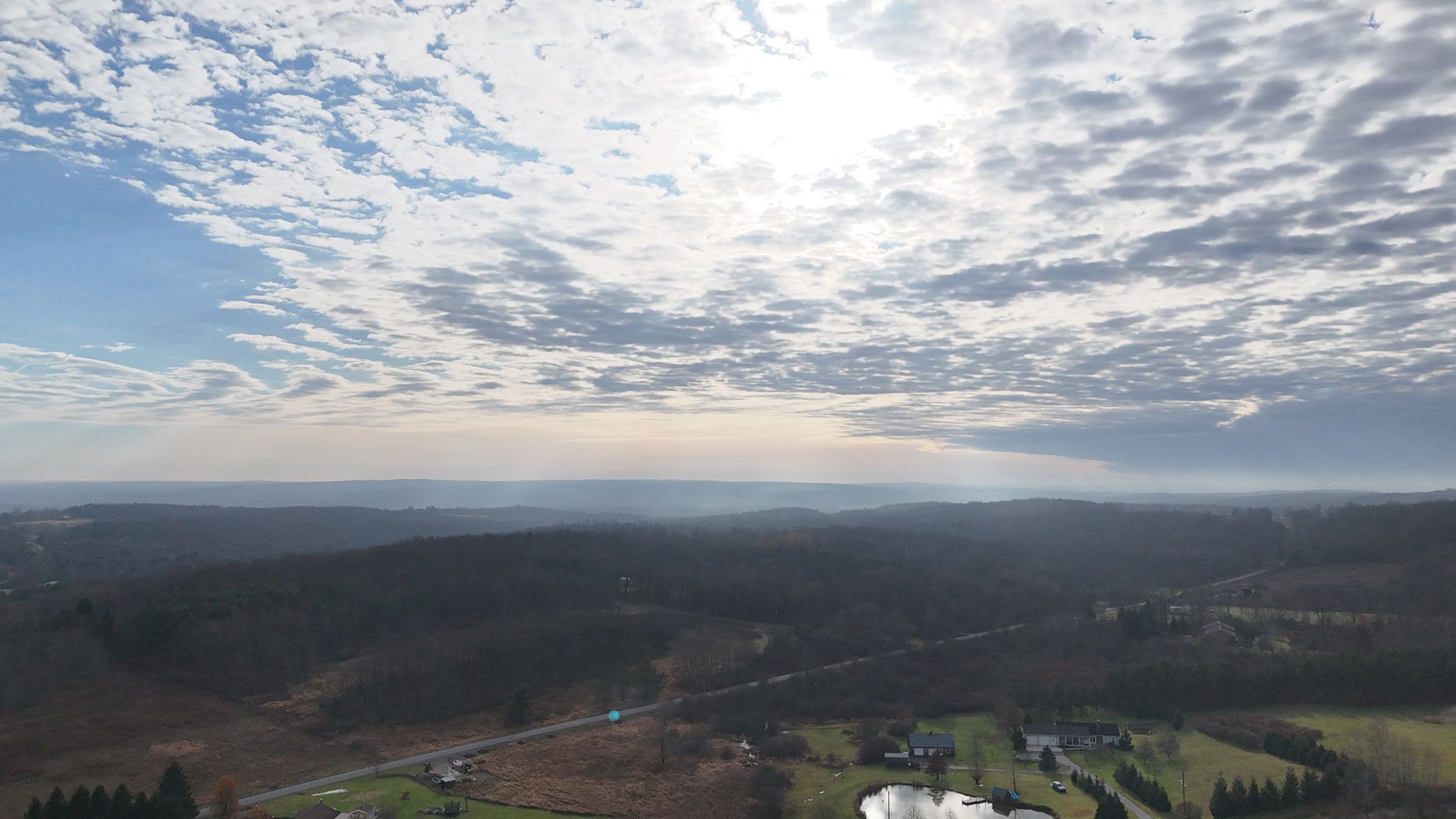 Overhead view of a landscape with cloudy skies and a distant mountain range under the sunlight.