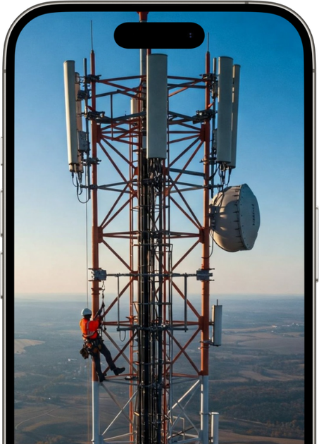 Worker climbing a tall cell tower against a blue sky.