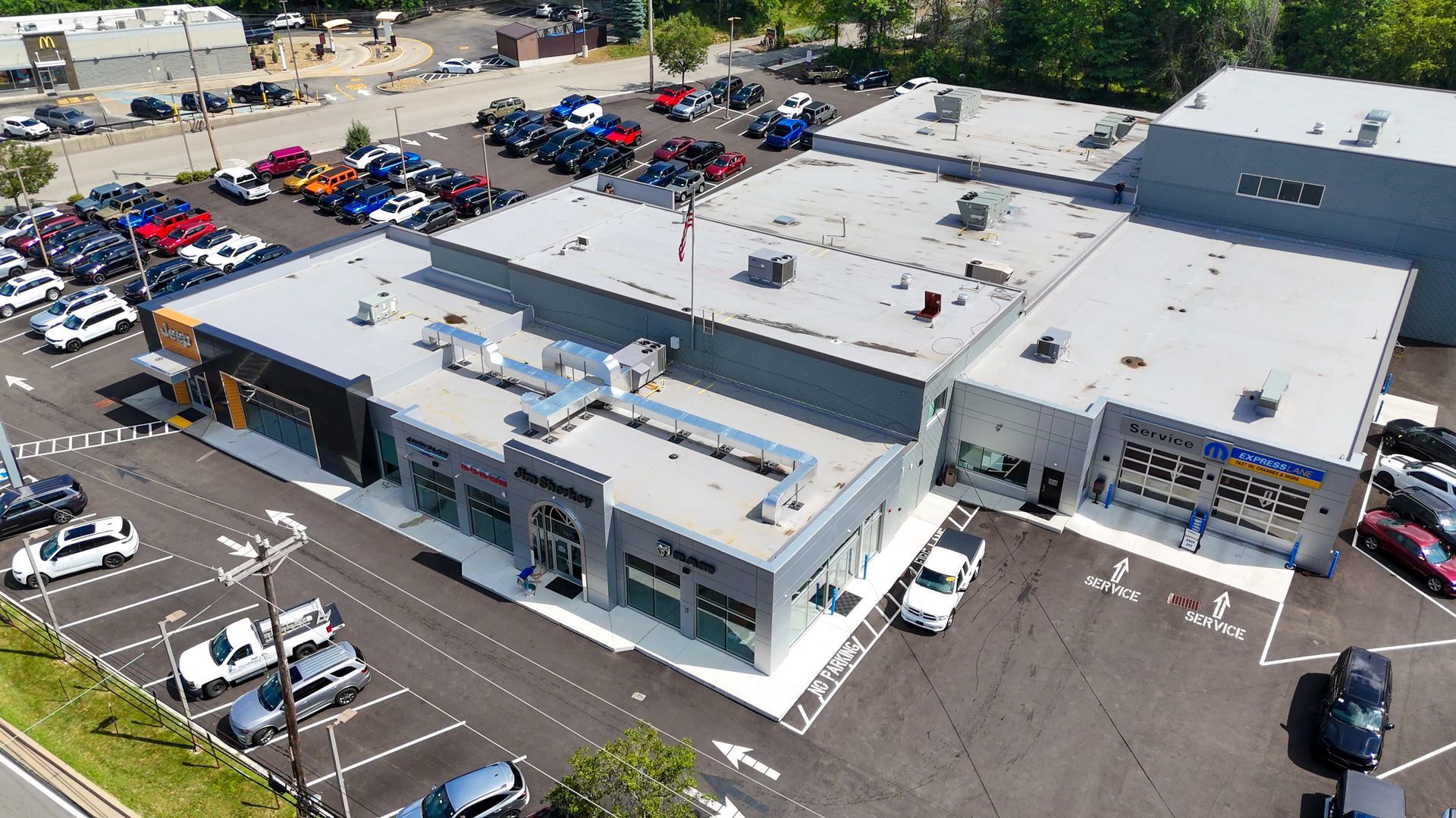 Aerial view of a car dealership with a variety of cars parked in front and a gray building.