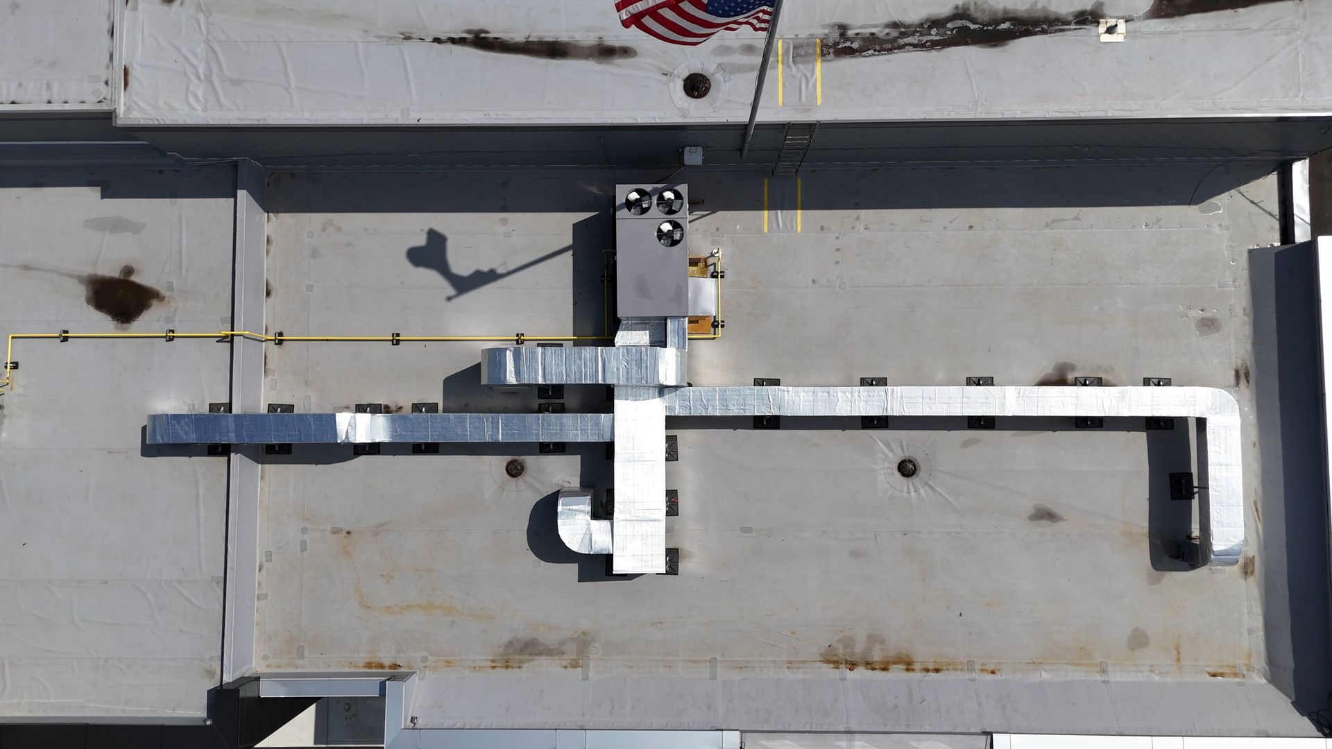 Overhead view of industrial ventilation ductwork, silver metal, on a gray surface, with a small American flag.