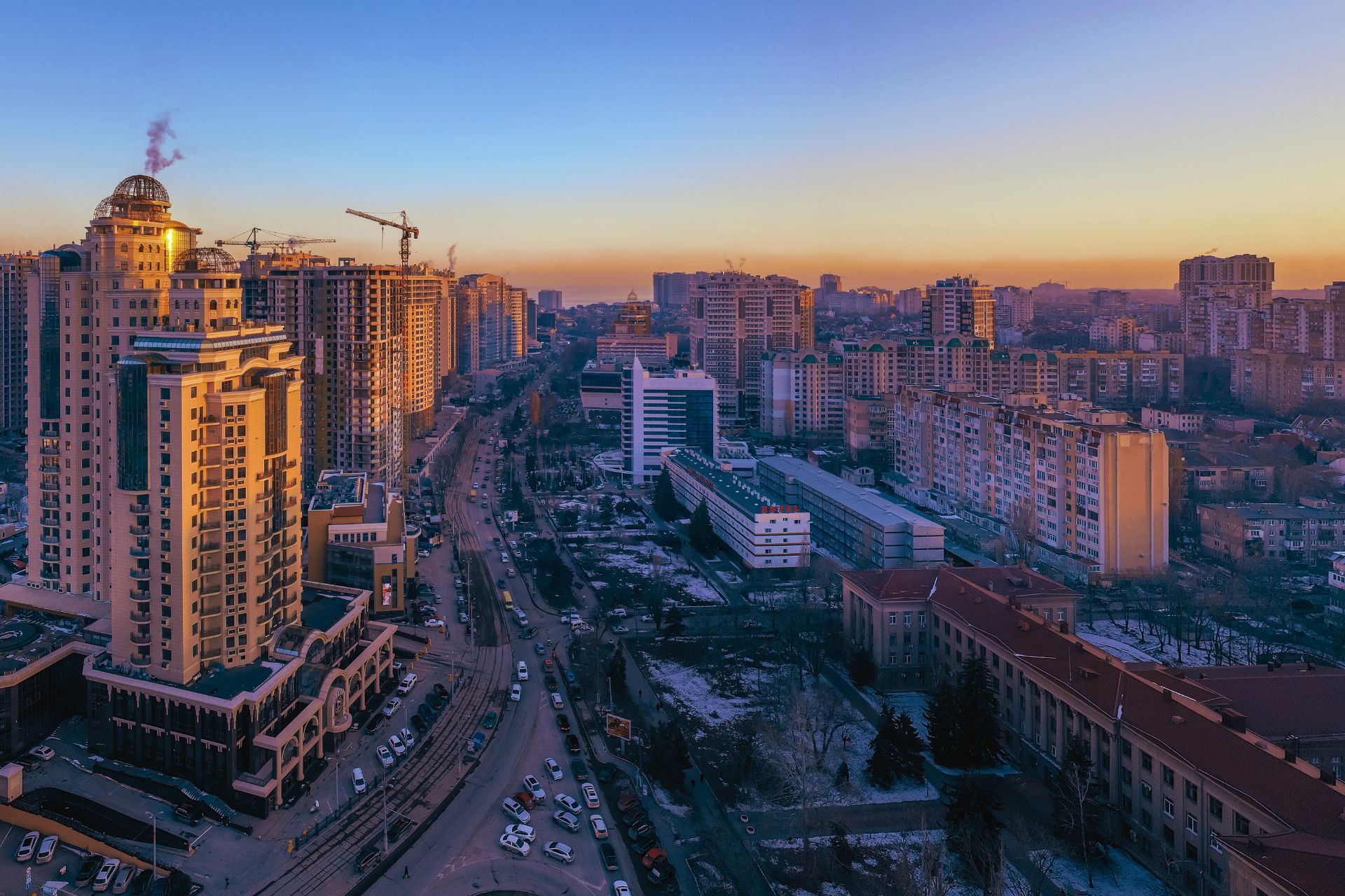 Cityscape at sunset. Tall buildings line a wide street. Golden sunlight reflects off structures; blue sky above.