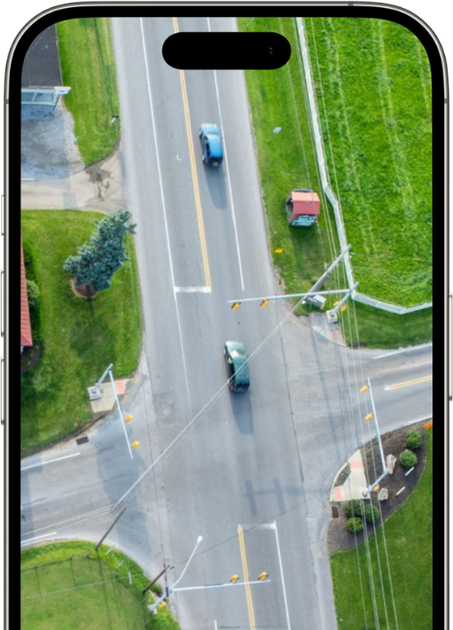 Aerial view of a road intersection with two cars, surrounded by green grass and small buildings.
