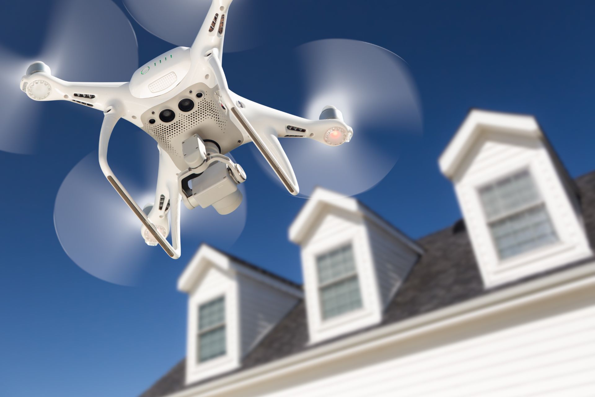 Drone flying over a residential building with dormer windows on a bright, sunny day.