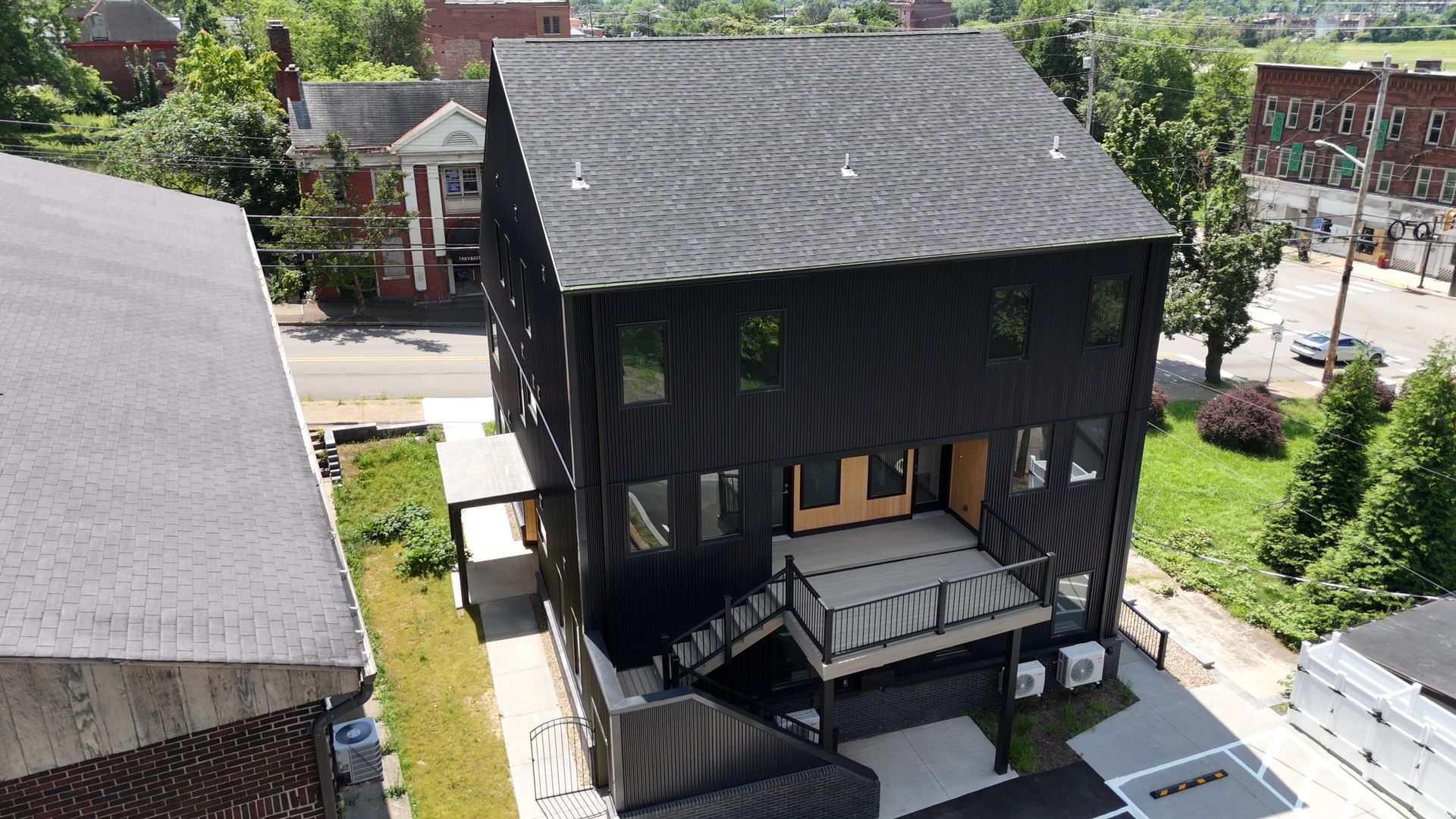 Black three-story house with porch and stairs, trees, and street in background.