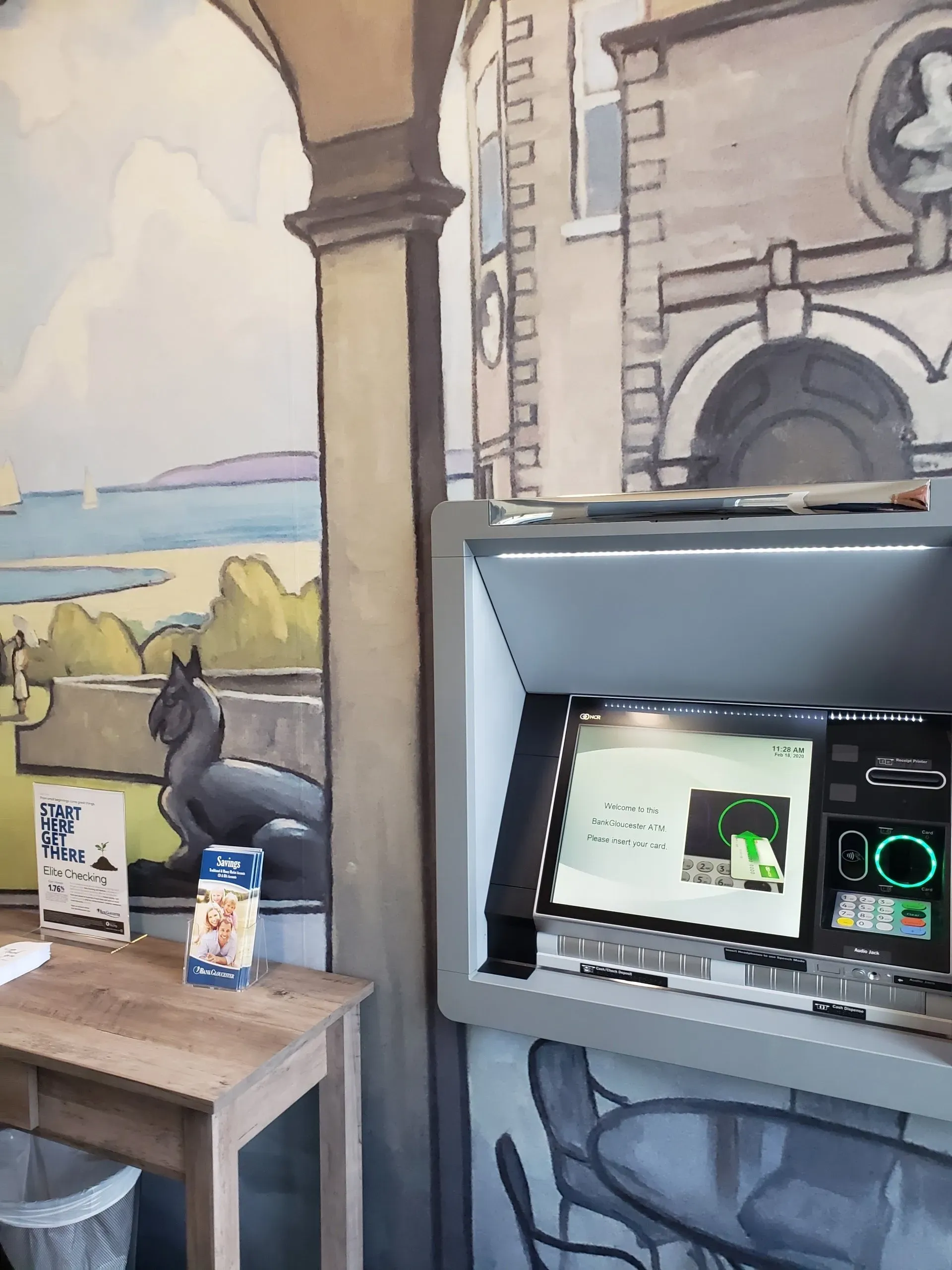 An atm machine with a painting on the wall behind it